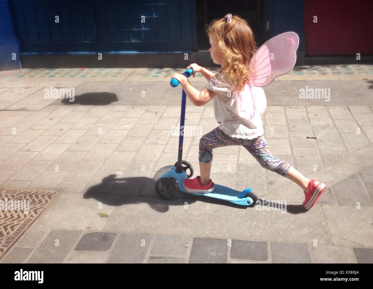 Großbritannien, England, London, Portrait eines Mädchens (2-3) mit Fee Flügel Reiten Scooter auf Stadt-Pflaster Stockfoto