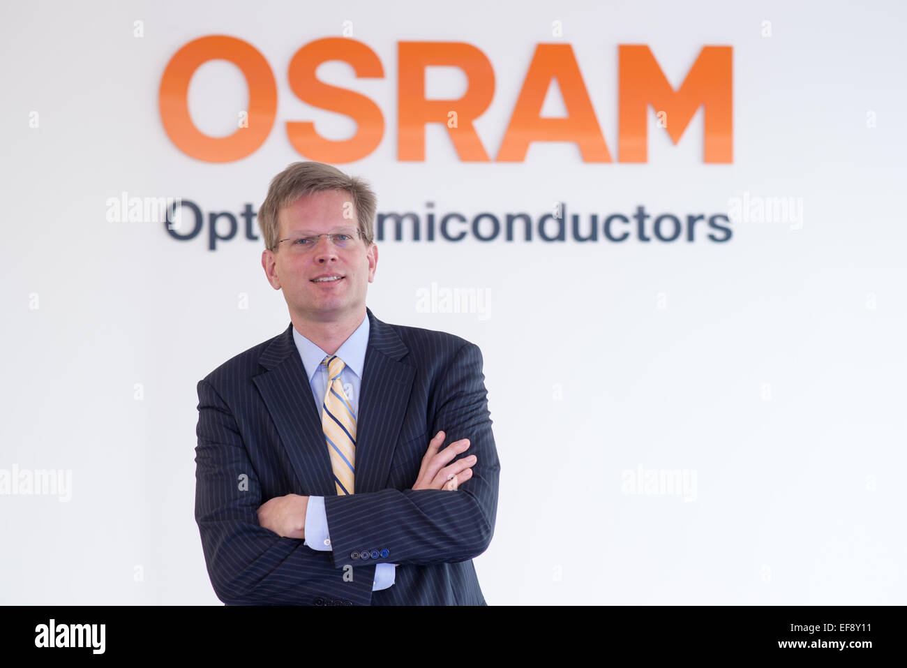 Der CEO der Halbleiter-Hersteller Osram Opto, Aldo Kamper, stand mit verschränkten Armen vor das Firmenlogo auf der Osram-Produktionsstätte in Regensburg, Deutschland, 26. Januar 2015. Foto: Armin Weigel/dpa Stockfoto