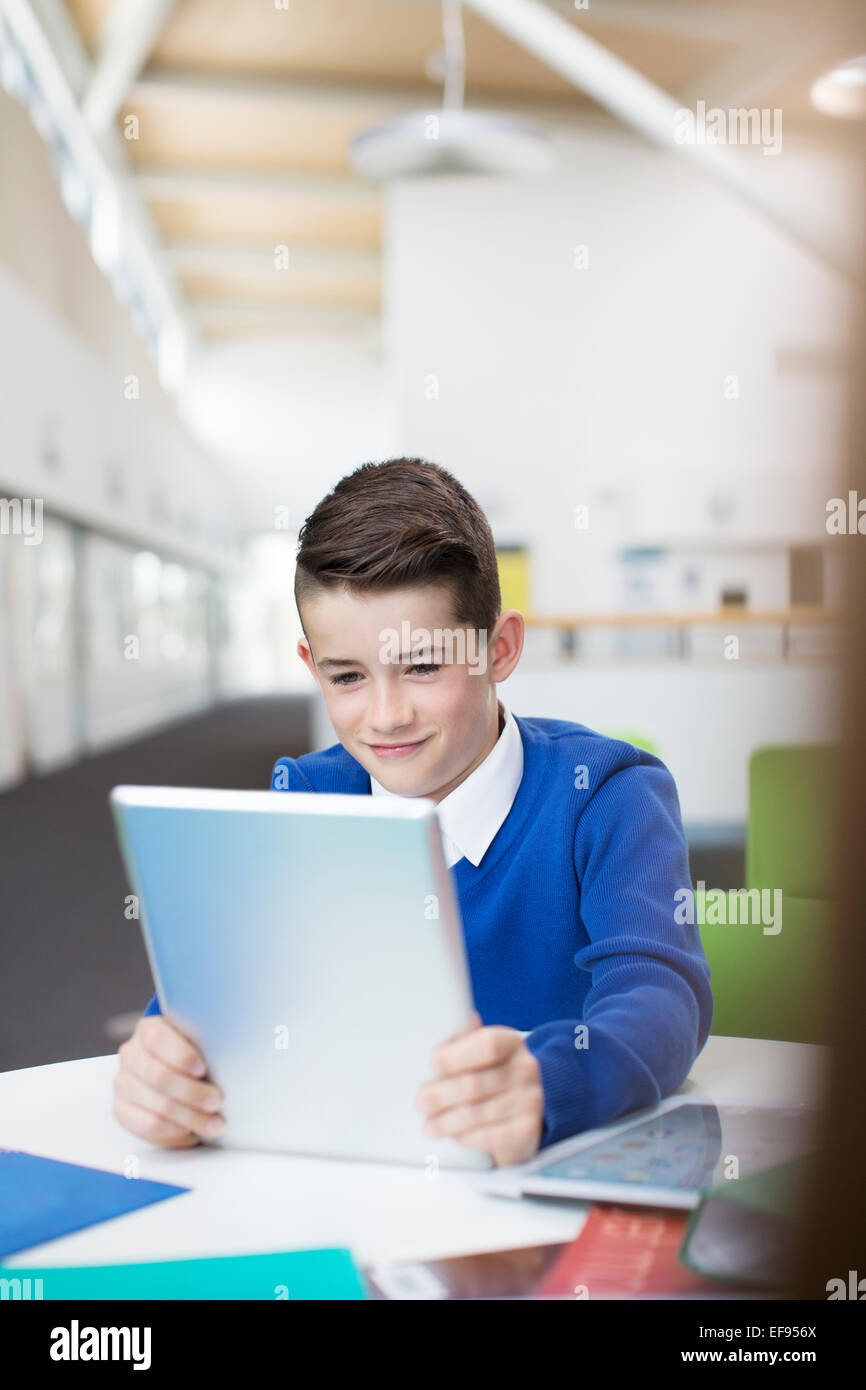 Lächelnd Grundschule junge tragen blaue Schuluniform holding digital-Tablette am Schreibtisch Stockfoto