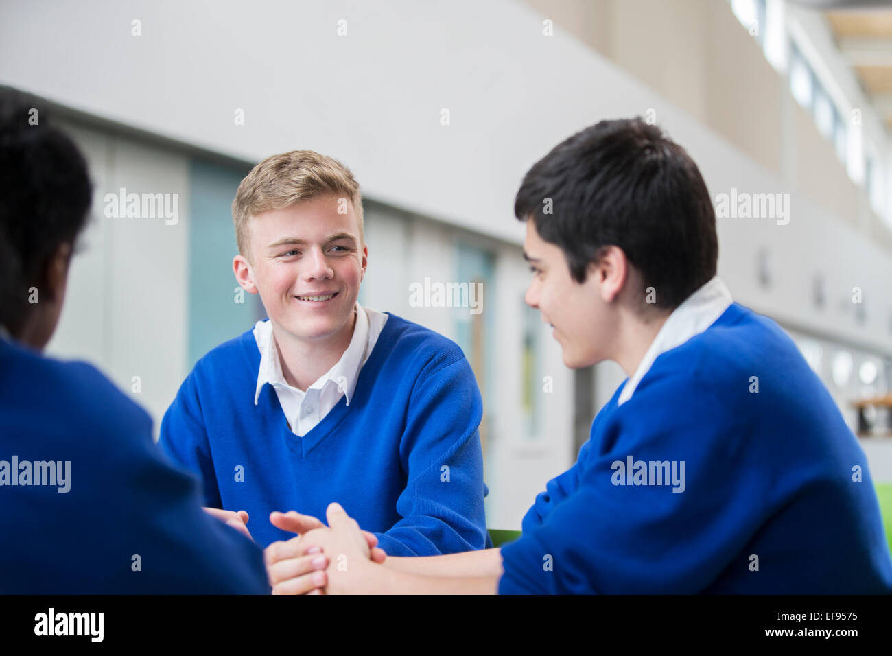 Drei männliche Studenten tragen blaue Schuluniformen sprechen im Korridor Stockfoto