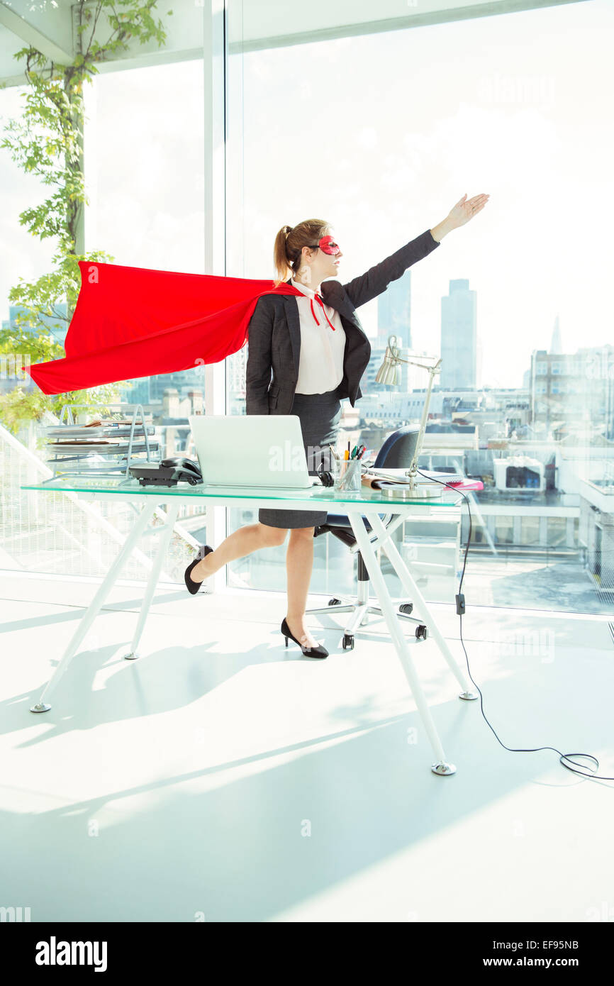 Geschäftsfrau in Cape und Maske im Büro fliegen wird vorbereitet Stockfoto