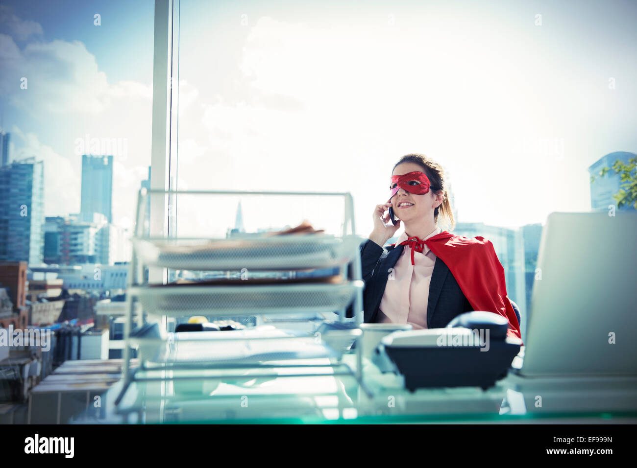 Geschäftsfrau in Cape und Maske Gespräch am Telefon am Schreibtisch Stockfoto