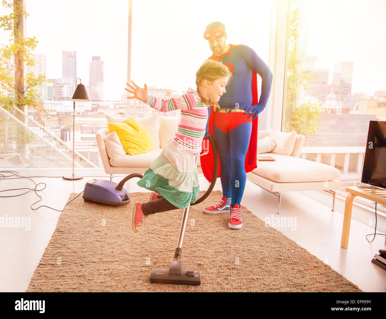 Superhelden-Vater Tochter springt im Wohnzimmer Staubsaugen Stockfoto