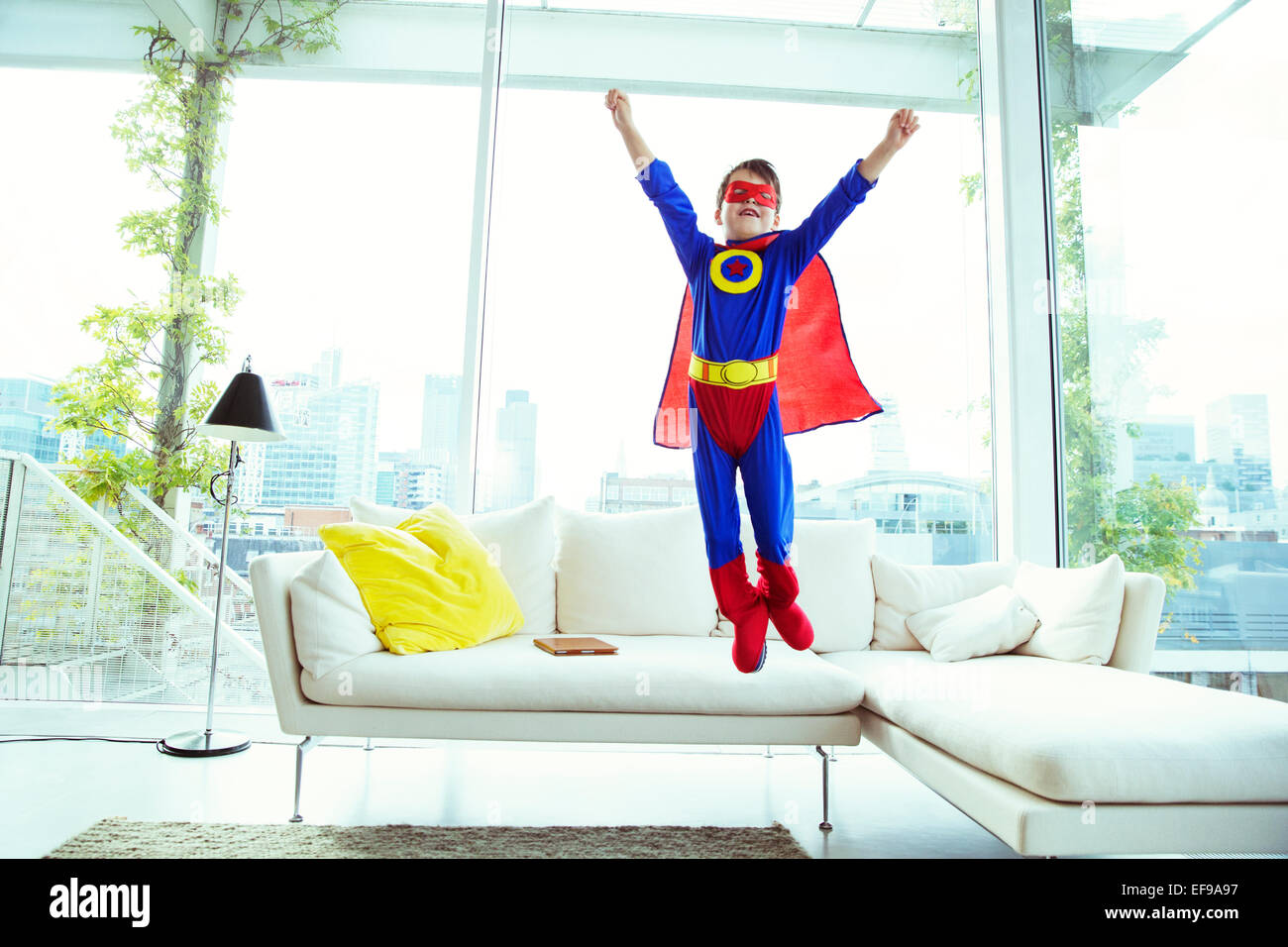Junge Superhelden abspringen Sofa im Wohnzimmer Stockfoto