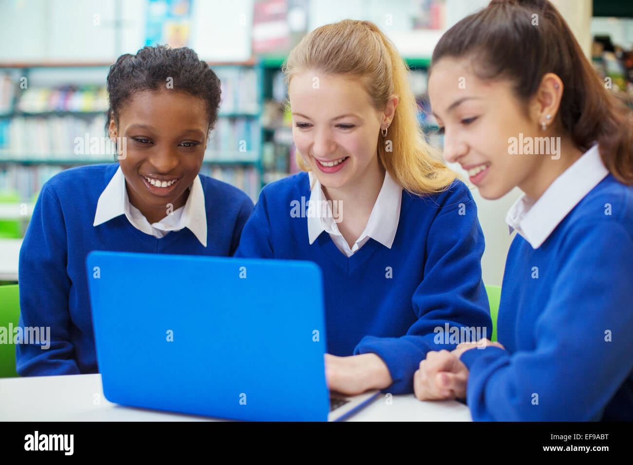 Drei Studentinnen tragen blaue Uniformen arbeiten am Laptop in der Bibliothek lächelnd Stockfoto