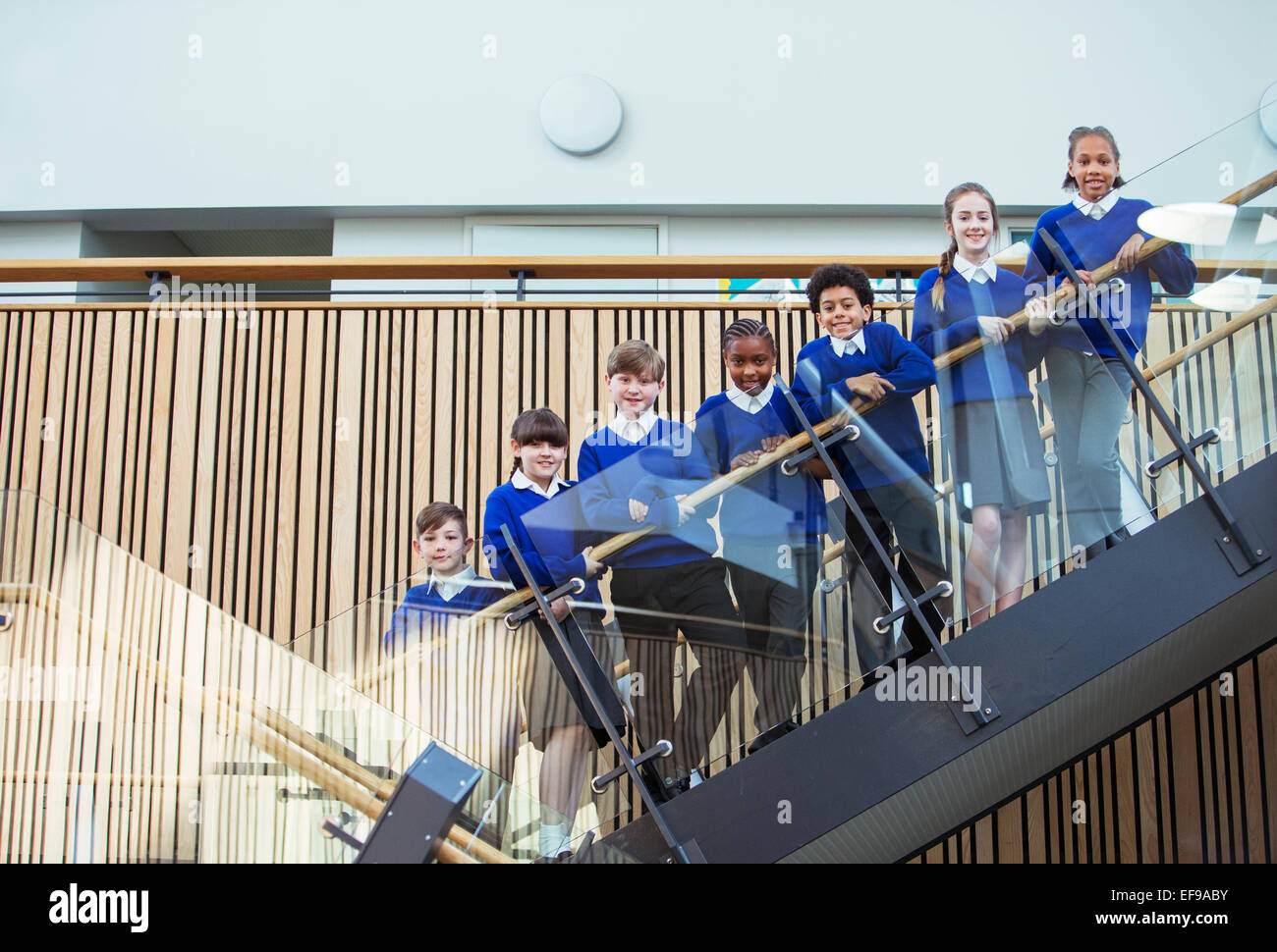 Porträt von Grundschülern tragen blaue Schule Uniformen stehen auf Schritte in der Schule Stockfoto