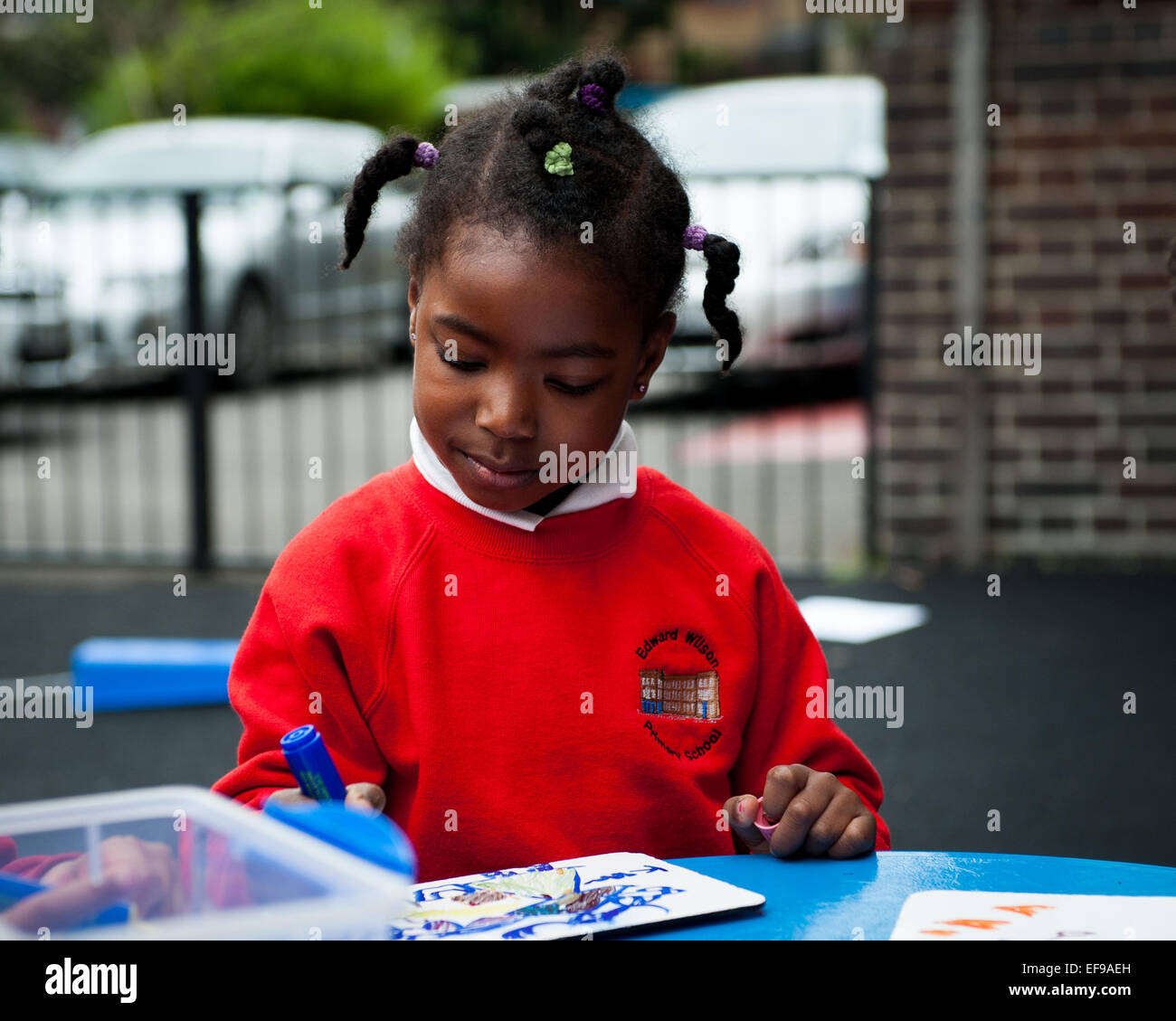 Schwarze Afro Caribbean Girl Spielen und zeichnen auf dem Spielplatz der Grundschule in London W2 Stockfoto