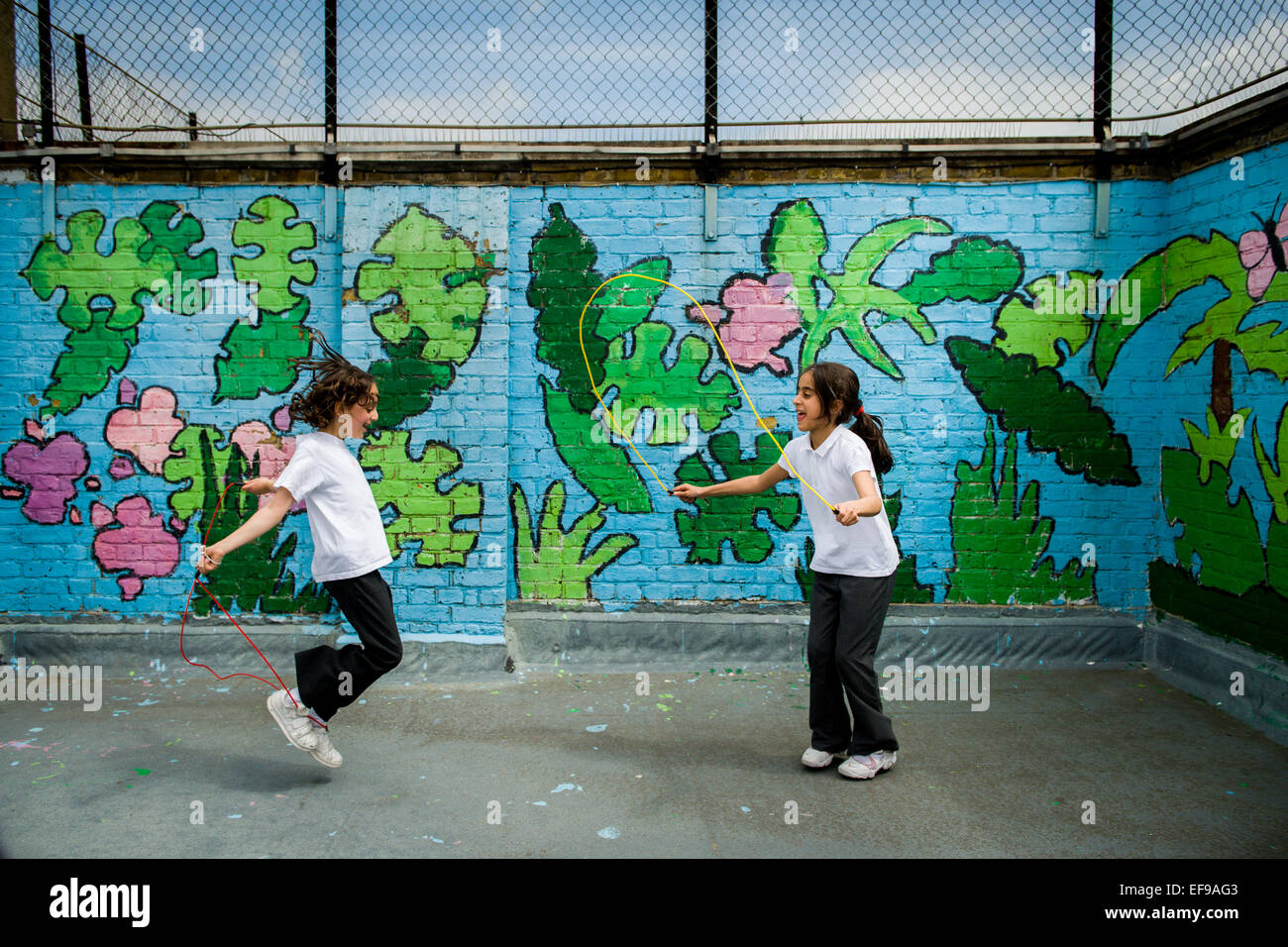 2 Mädchen, die auf dem Schulspielplatz mit Graffigeblättern überspringen Stockfoto