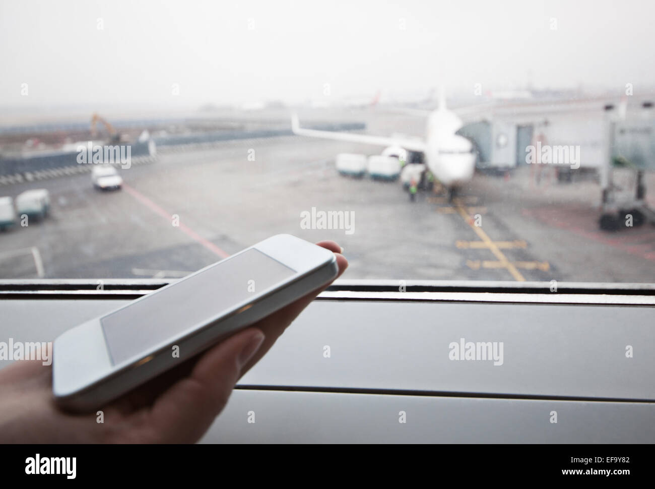 Hand mit Smartphone durch das Fenster am Flughafen Stockfoto
