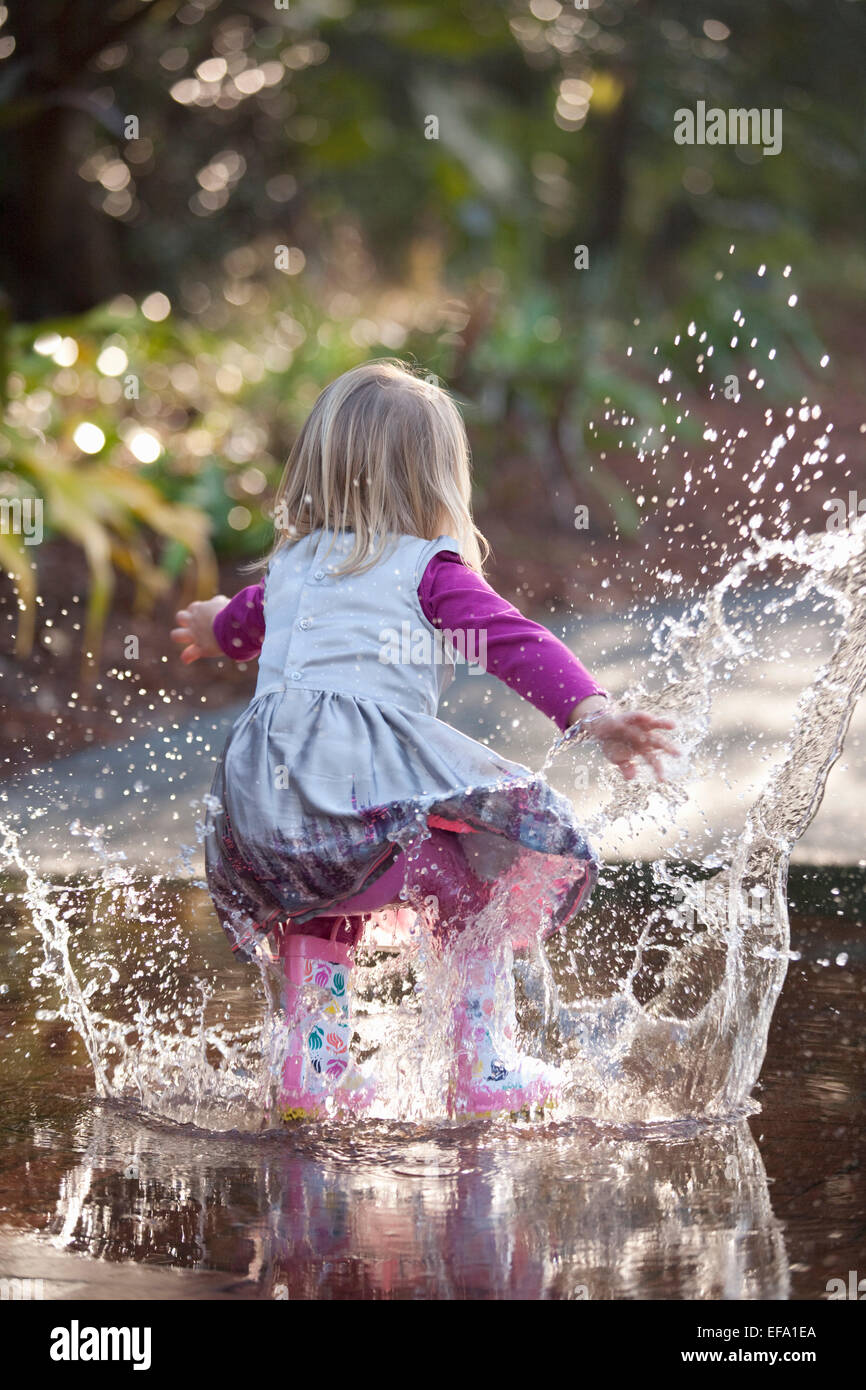 Ein kleines Gummistiefel Mädchen tragen Spritzer in einer Pfütze auf der Straße. Stockfoto