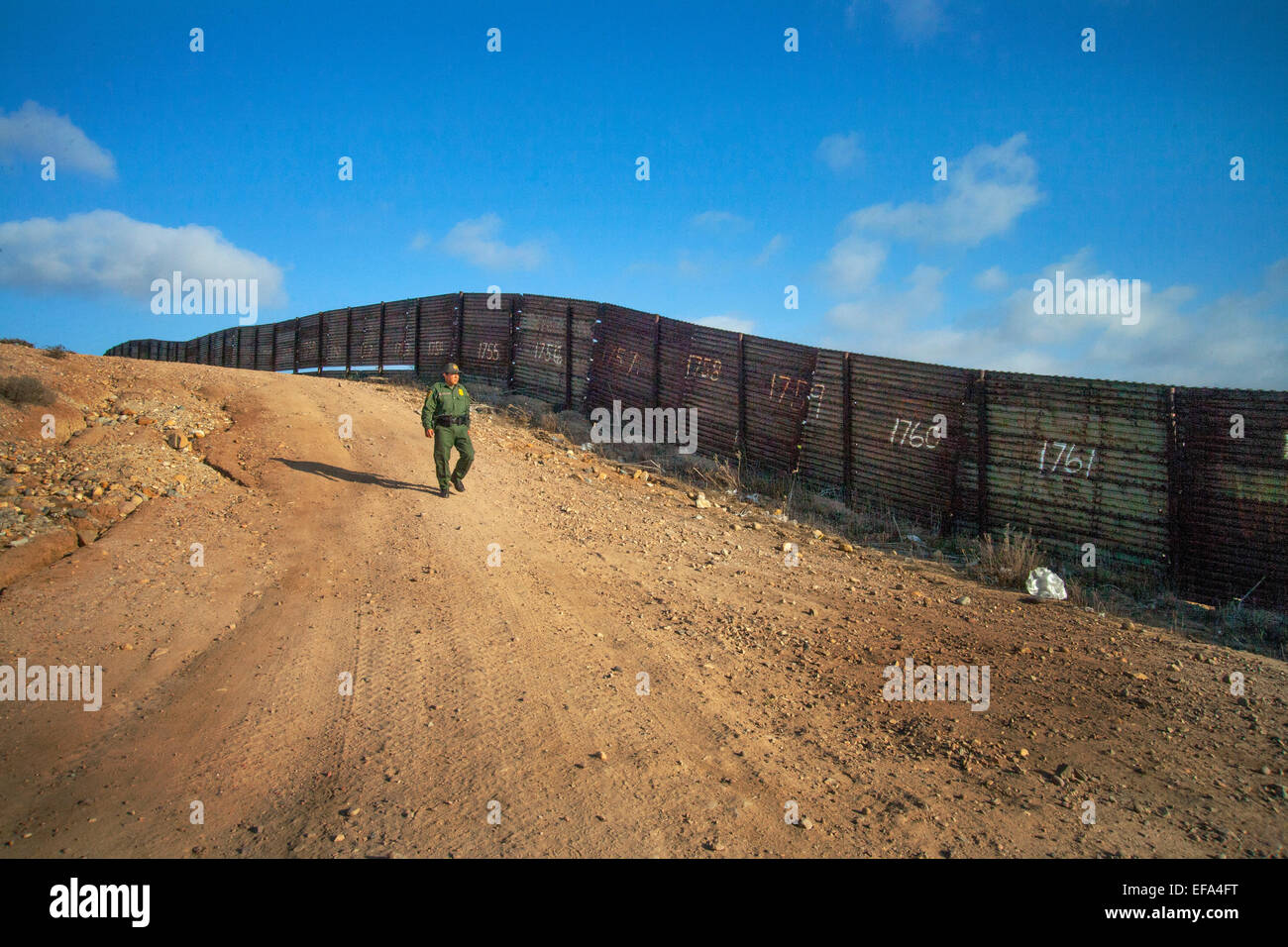 Polizeilichen Bereich "Bunker Hill" von der U.S./Mexico Grenze in der Nähe von Tijuana, Spaziergänge ein hispanischen Border Patrol Officer entlang des Sicherheitszauns. Die Border Patrol ist Teil des US Department of Homeland Security. Beachten Sie die nummerierte Tafeln auf Zaun, Standort zu ermitteln. Stockfoto