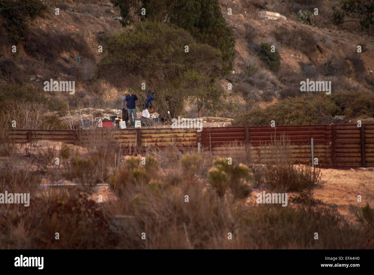 Um ein Lagerfeuer hinter dem internationalen Zaun in Tijuana an der U.S./Mexico Grenze eine Gruppe illegaler Einwanderer wartet Nacht versucht Überfahrt in die USA Stockfoto