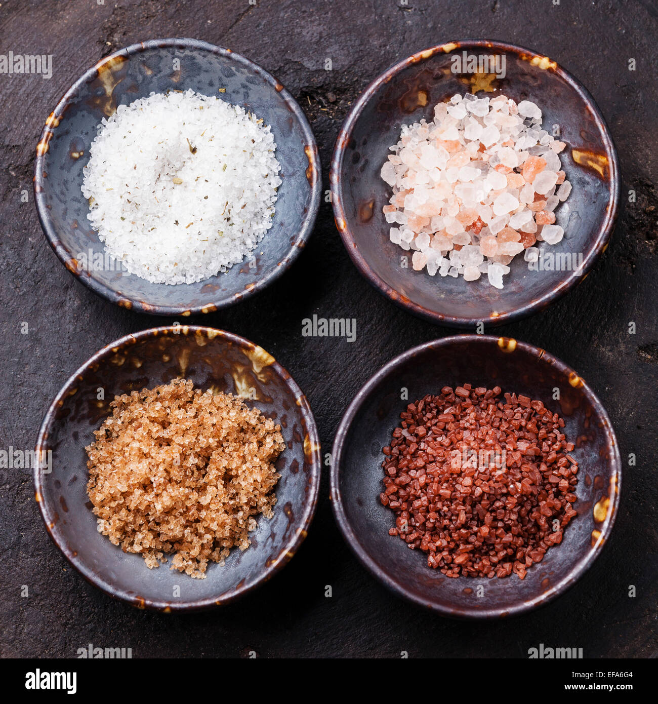 Verschiedene Arten von Lebensmitteln grobes Salz in Keramikschalen auf dunklem Hintergrund Stockfoto