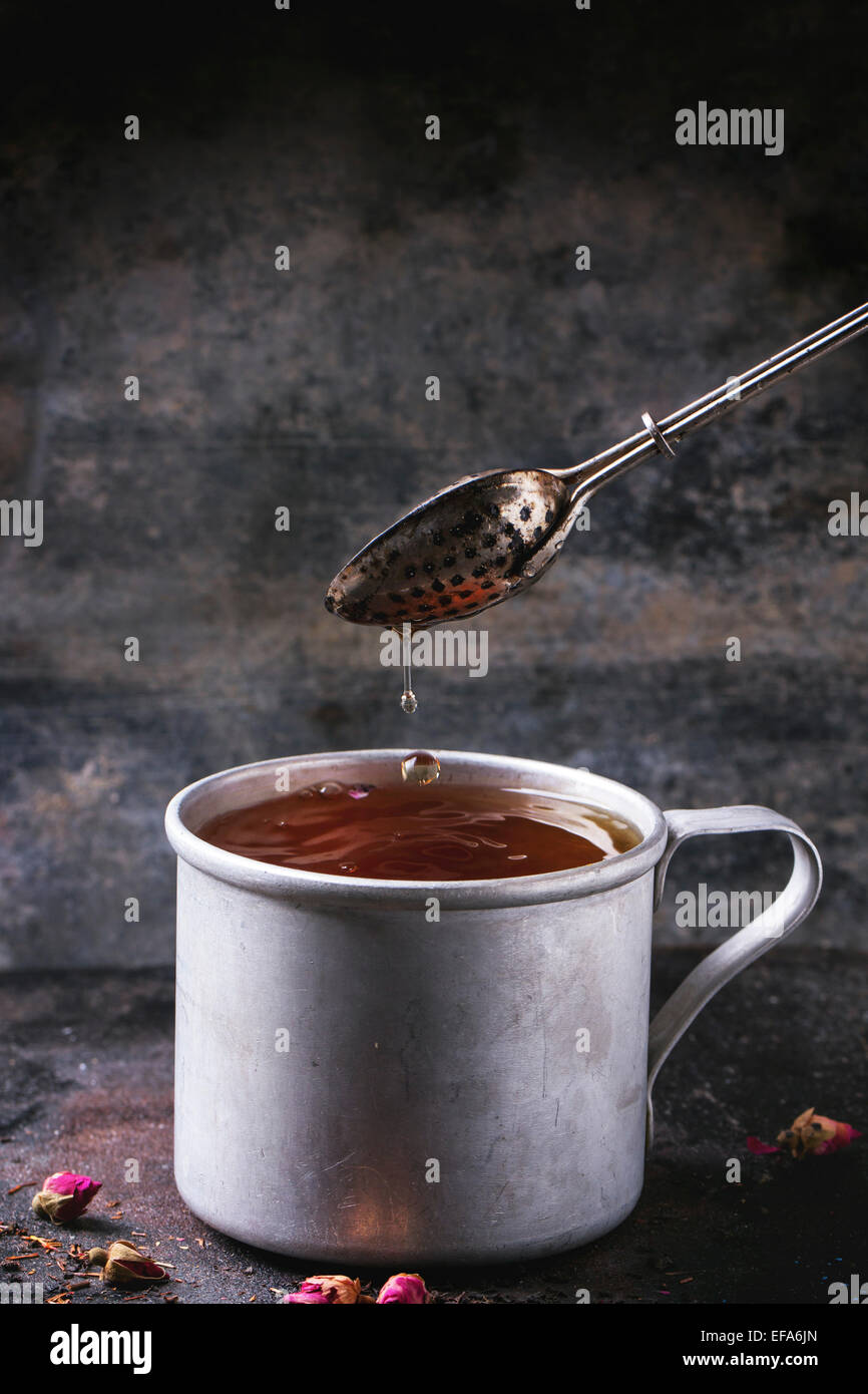 Vintage Alu-Becher mit fließendem heißen Tee mit Teesieb auf dunklem Hintergrund Stockfoto