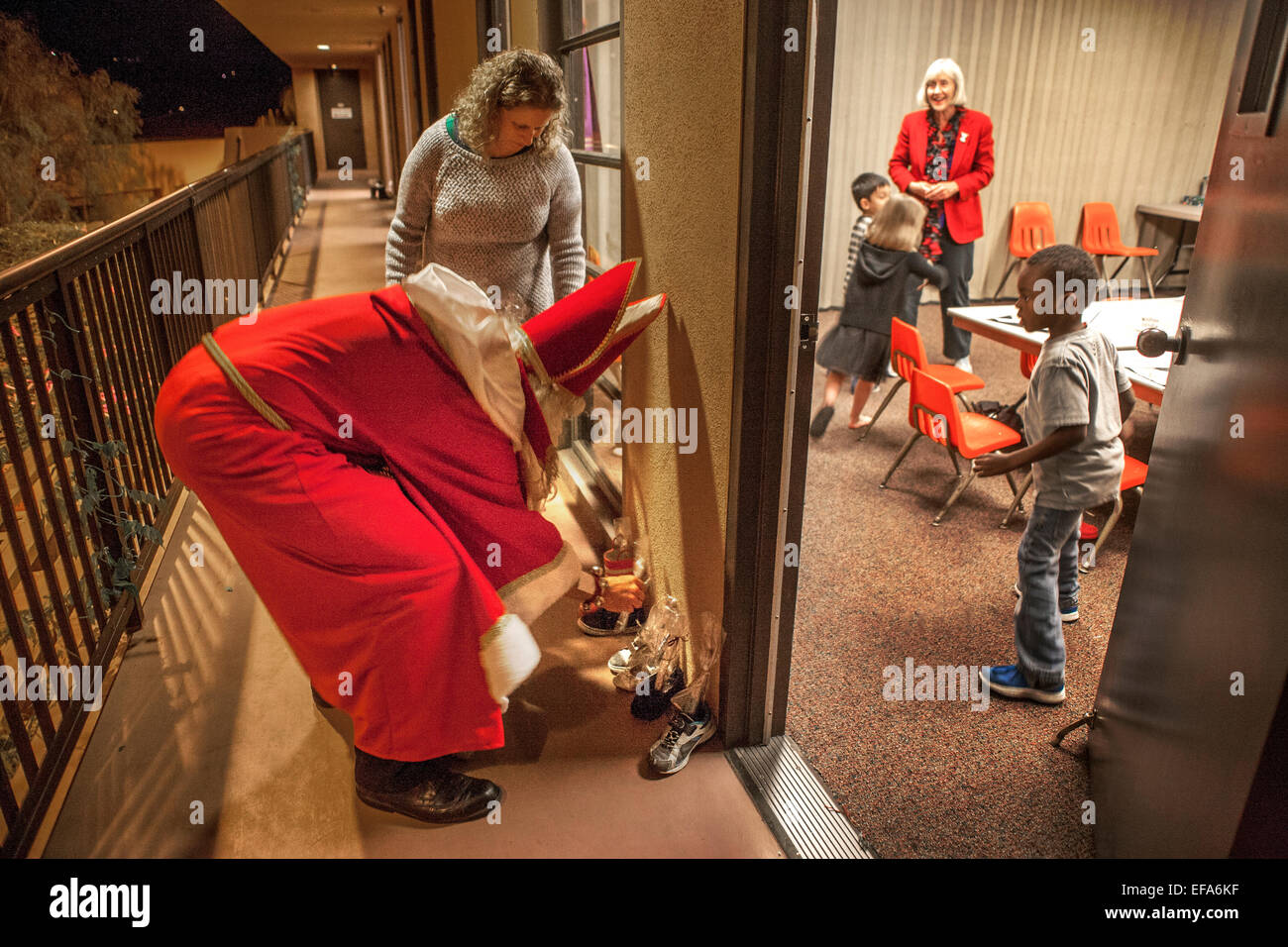 Katholische Kirche St. Timothy, Laguna Niguel, CA, ein Gemeindemitglied als St. Nikolaus ihre Schuhe draußen ein Bastelraum im Advent für Kinder Weihnachtsgeschenke stellenweise gekleidet. Hinweis Kind beobachten. Stockfoto