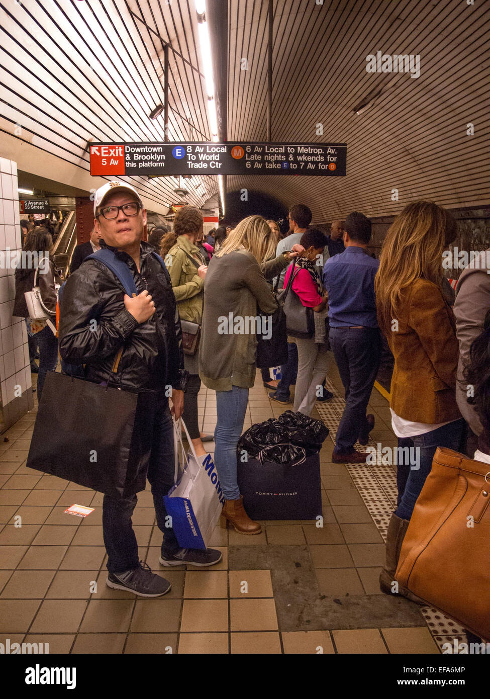 Gemischtrassig Passagiere warten auf einen Zug auf einer u-Bahn-Bahnsteig in New York City. Beachten Sie die Beschilderung. Stockfoto