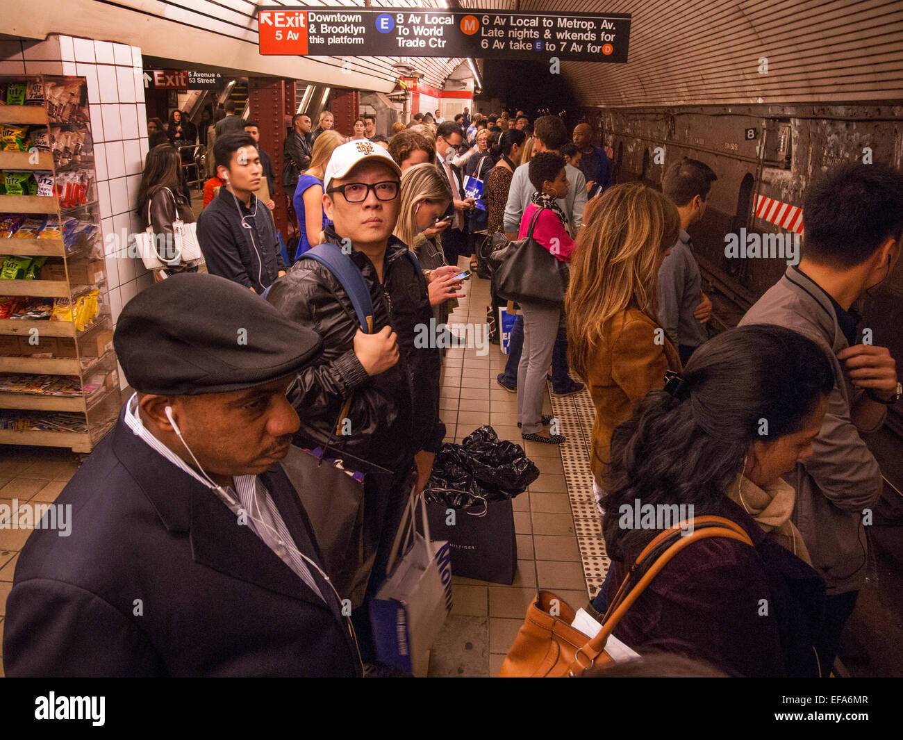 Gemischtrassig Passagiere warten auf einen Zug auf einer u-Bahn-Bahnsteig in New York City. Beachten Sie die Beschilderung. Stockfoto