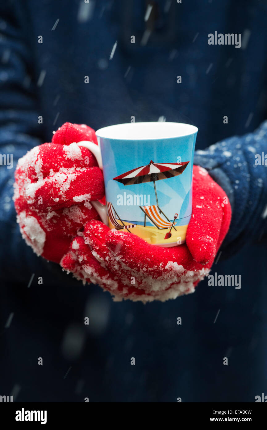 Rote behandschuhten Hände halten ein warmes Getränk im Schnee Stockfoto