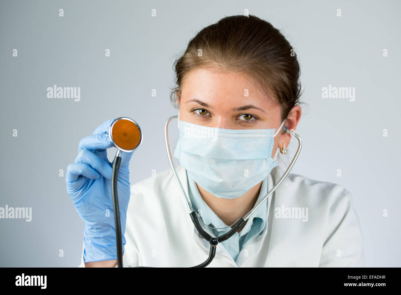 junge Ärztin trägt Latex-Handschuhen und Maske und hält ein Stethoskop Stockfoto