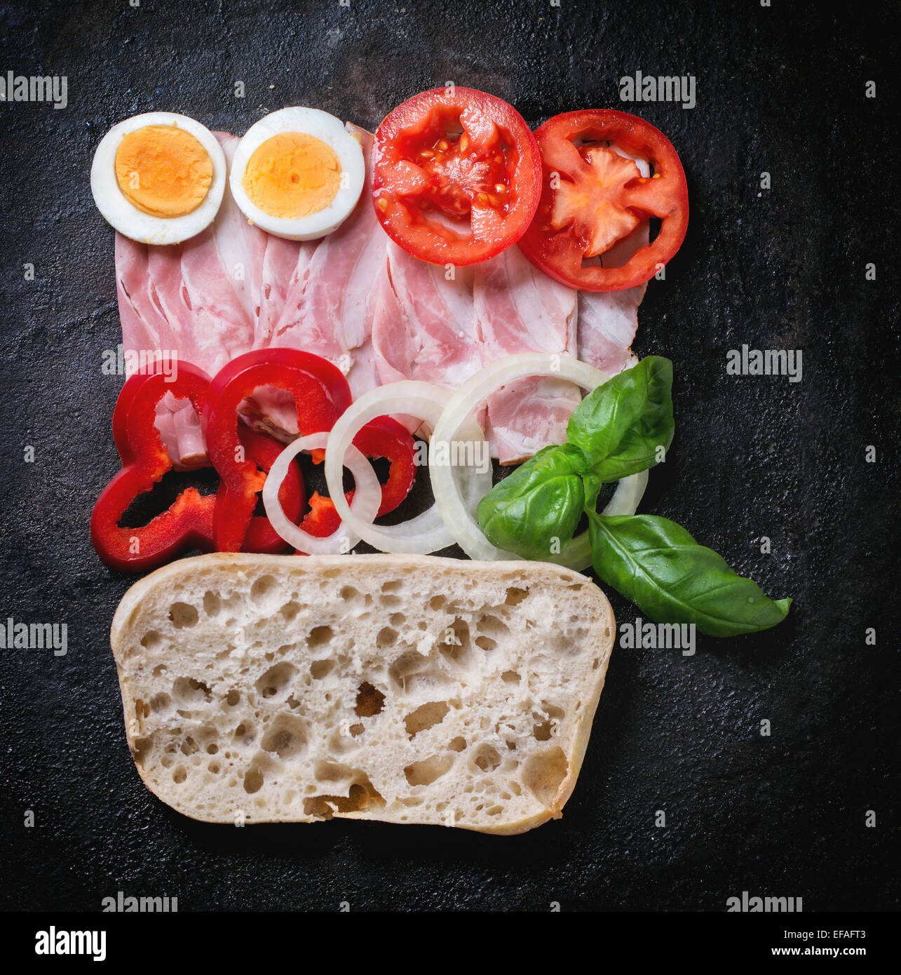 Zutaten für Sandwich mit Schinken, Eiern und Gemüse auf schwarzem Hintergrund. Ansicht von oben Stockfoto