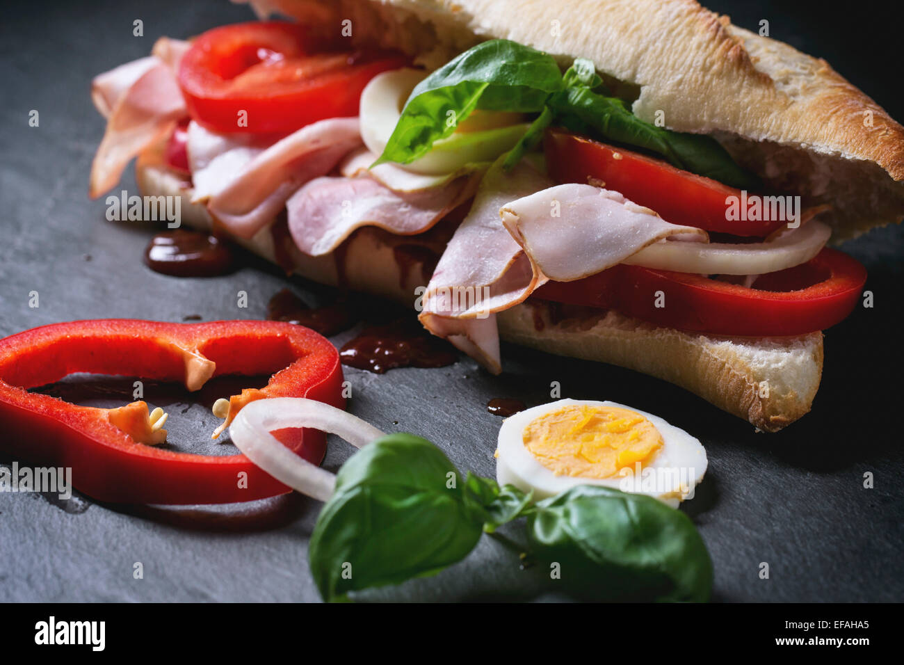Sandwich mit Schinken, Eiern, Gemüse und Ketchup auf schwarzem Hintergrund. Serien ansehen Stockfoto