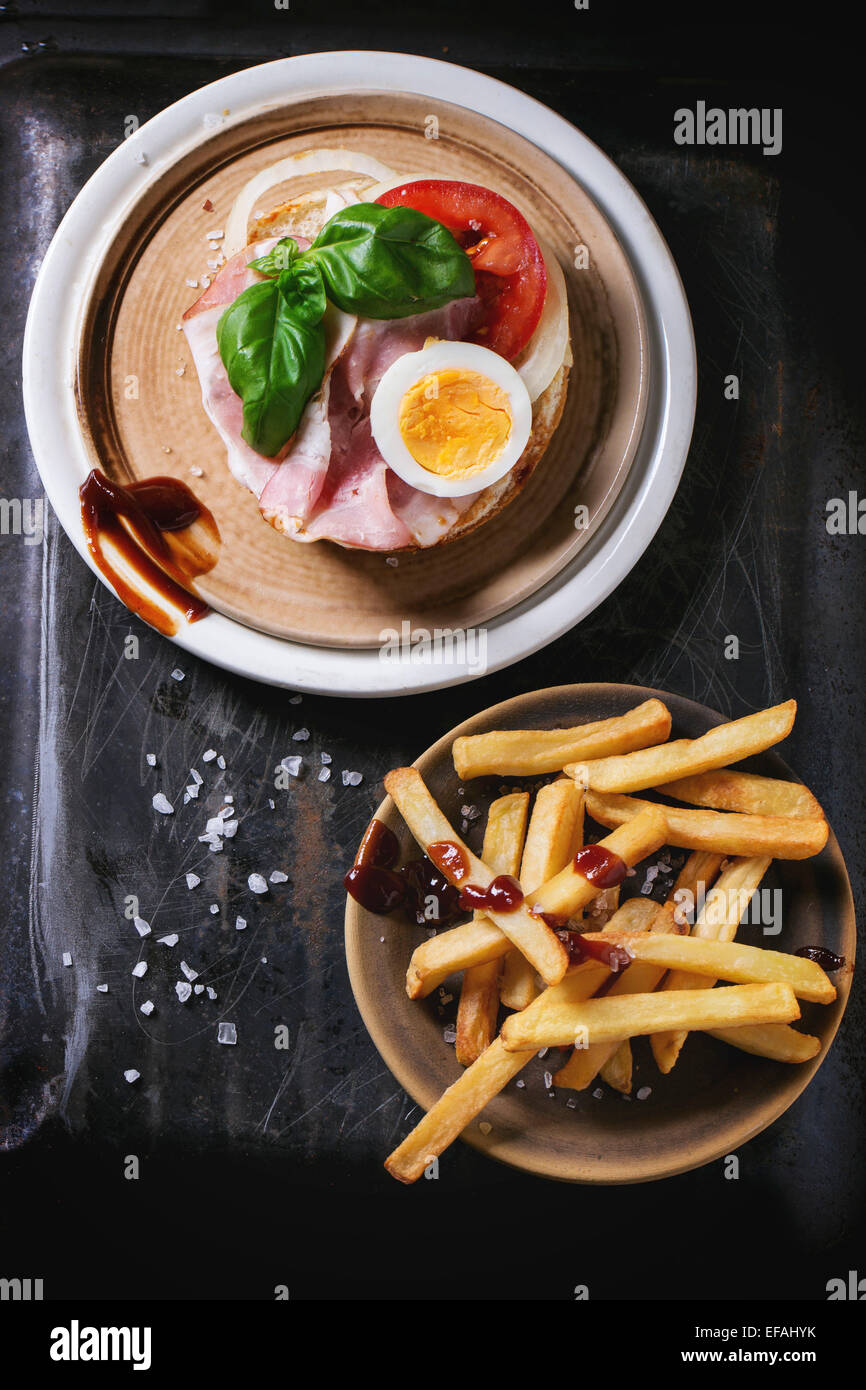 Keramikplatte mit Sandwich mit Schinken, Eiern, Gemüse und Ketchup, serviert mit Pommes frites über schwarzen Metall Hintergrund. Top vi Stockfoto
