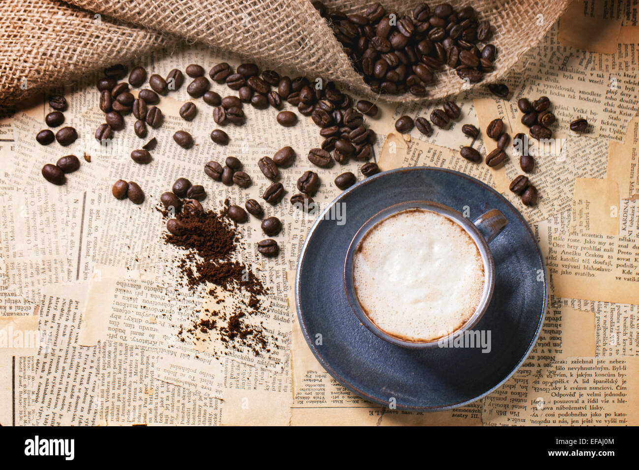 Blaue Keramik Tasse Cappuccino mit gerösteten Kaffeebohnen über alte Zeitung. Ansicht von oben. Stockfoto