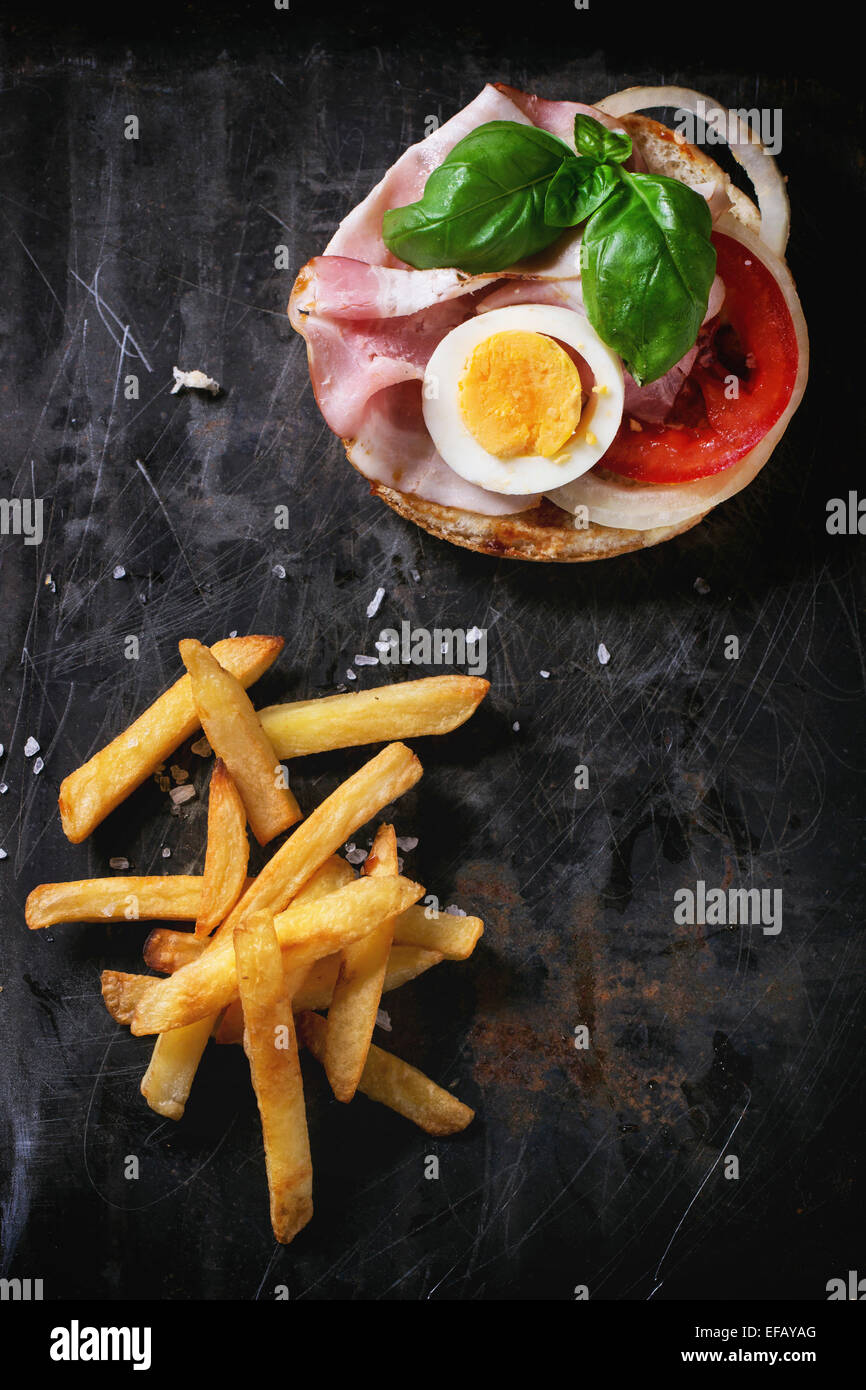 Sandwich mit Schinken, Eiern, Gemüse und Ketchup, serviert mit Pommes Frites auf schwarzem Hintergrund. Serien ansehen Stockfoto