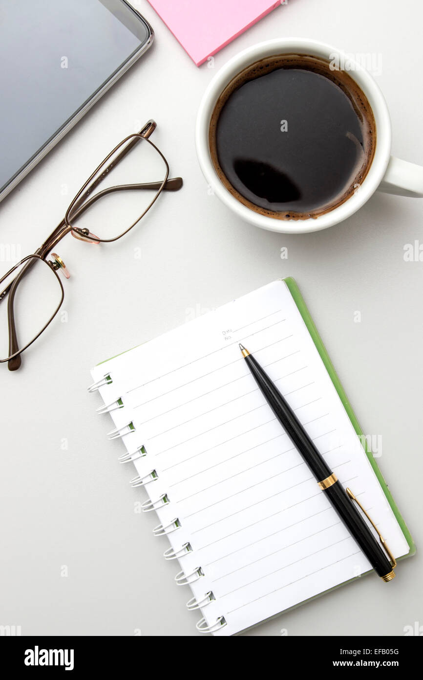 Büro-Desktop mit Kaffee, Notizblock und Gläser. Von oben Stockfoto