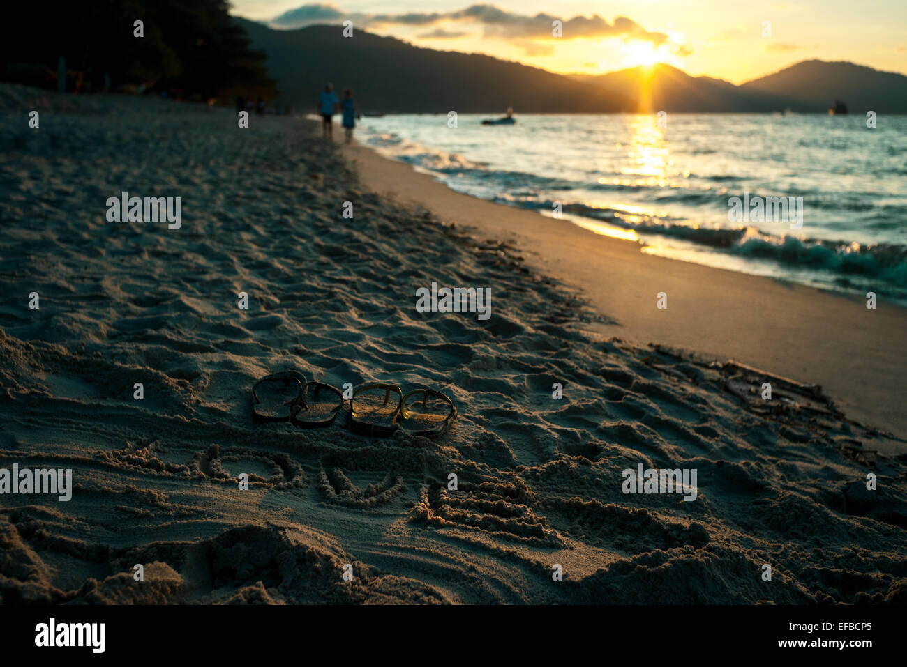 Sand schreiben des Wortes Liebe mit Sandalen am Meer bei Sonnenuntergang Stockfoto