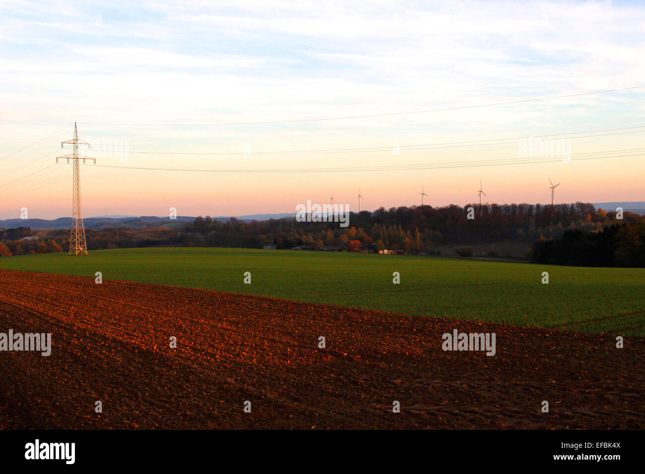 Feld, Power Line und Windturbinen bei Sonnenuntergang. Niedersachsen, Deutschland Stockfoto