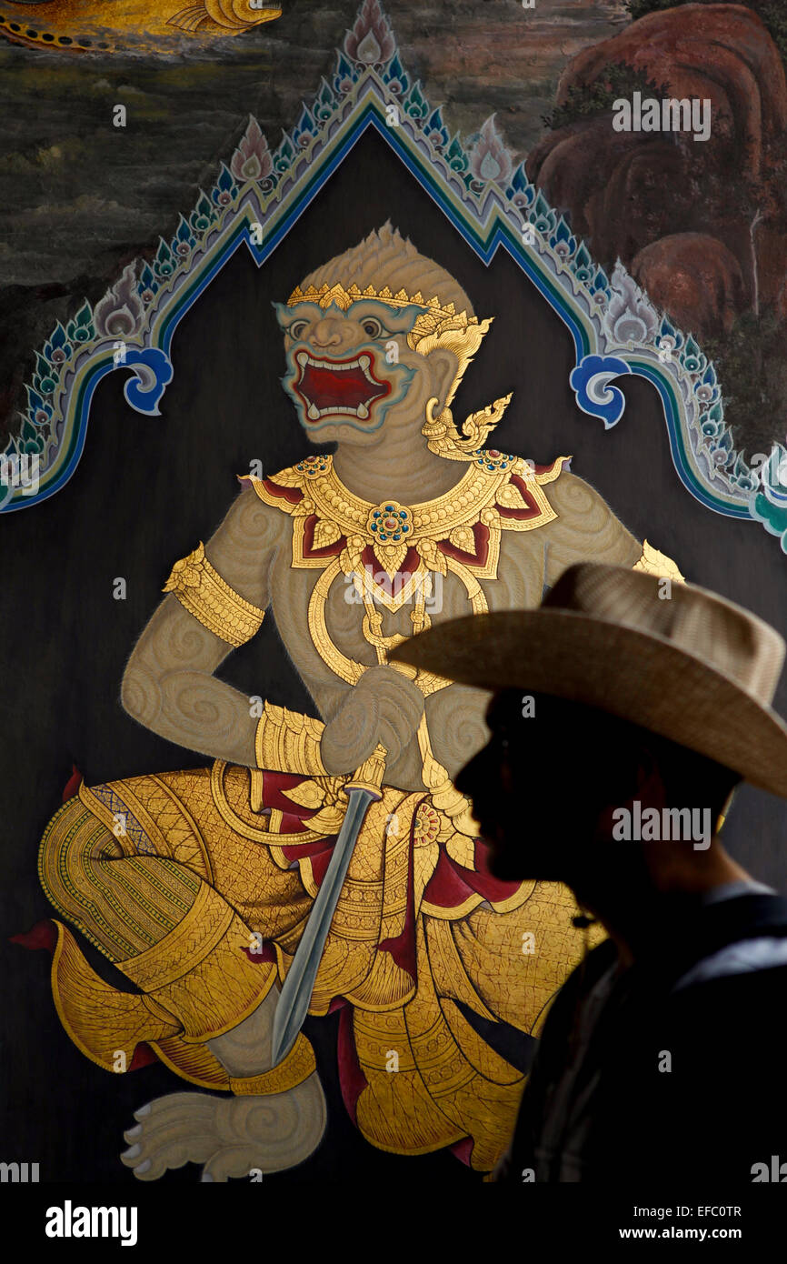Ein Besucher wird im Hintergrund eines Wandgemäldes an einer Eingangswand im Grand Palace Komplex in Bangkok, Thailand, fotografiert. Stockfoto