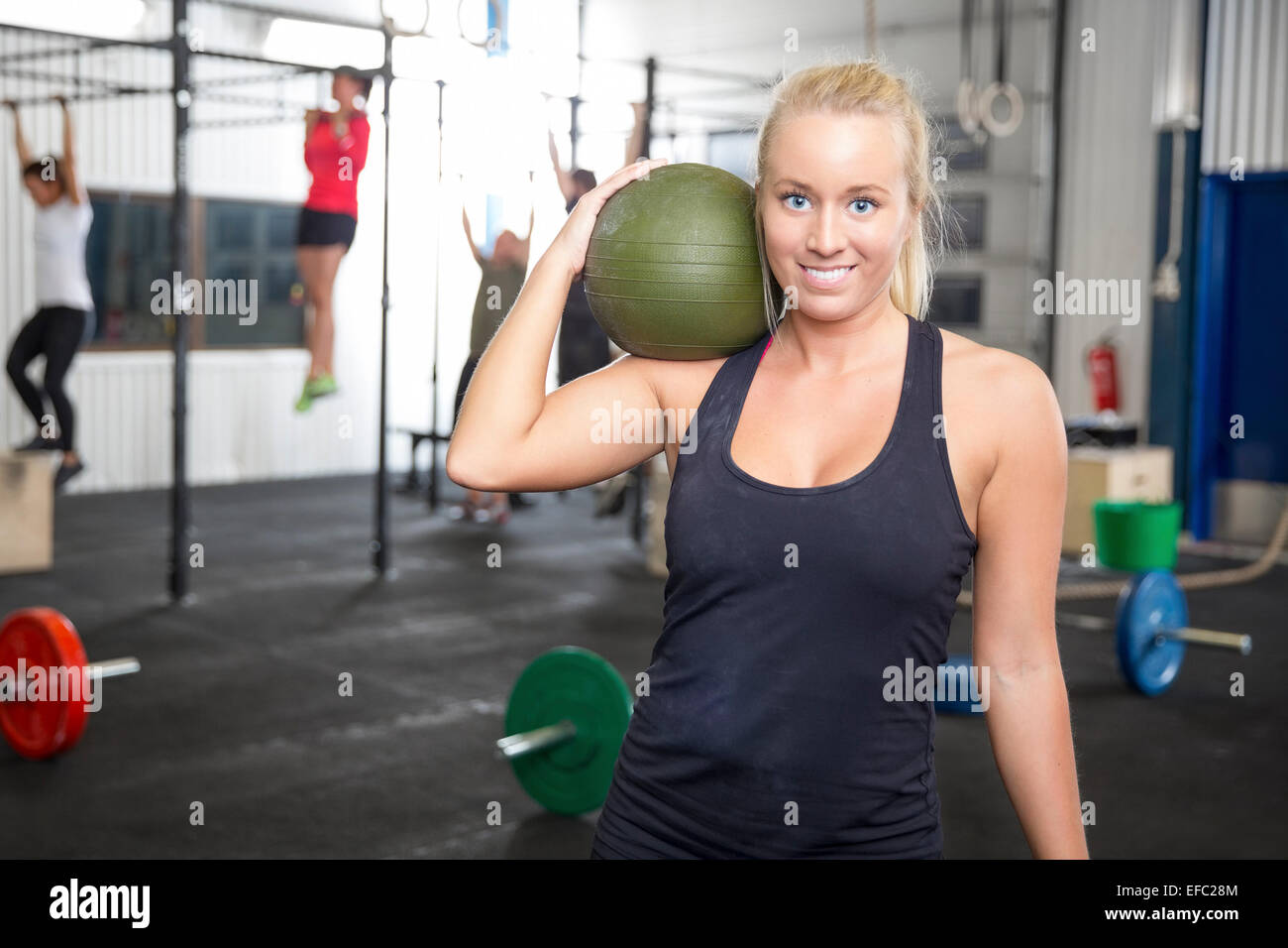 Lächelnde blonde Frau mit Slam-Ball im Fitness-Studio Stockfoto