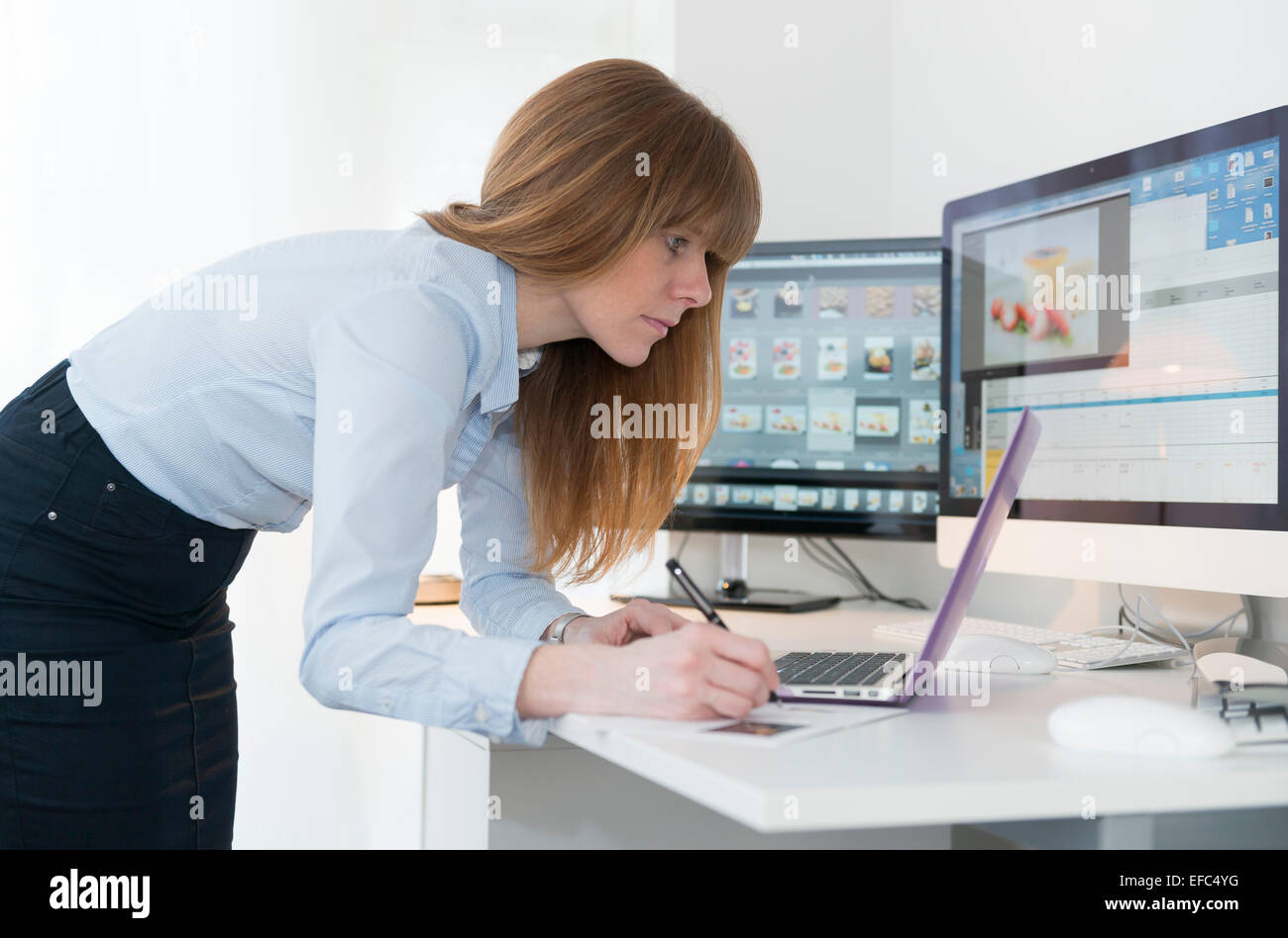 Eine Frau arbeitet in einem Büro am Schreibtisch, Bearbeitung einer Zeitschrift. Stockfoto