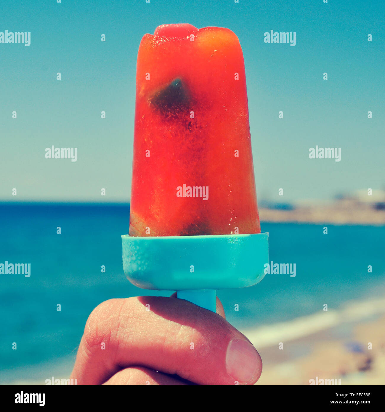 Nahaufnahme der Hand eines jungen Mannes mit einem hausgemachten Eis pop am Strand, mit einem Filter-Effekt Stockfoto