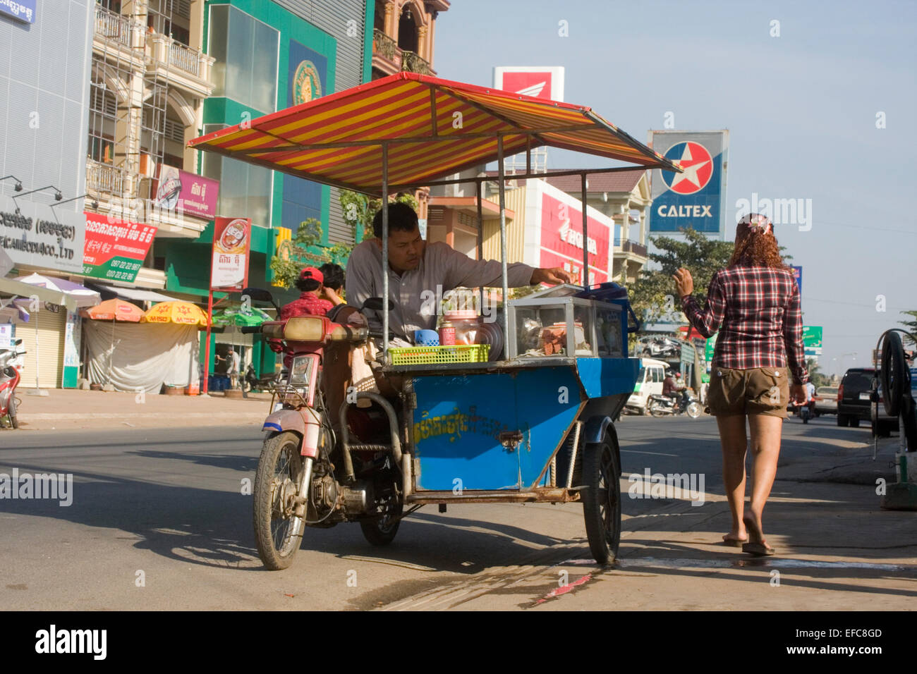 Eine Frau winkt zu einem Mann verkaufen Suppen von einem mobilen Lebensmittel Karren auf eine Stadt in Kampong Cham, Kambodscha Straße. Stockfoto