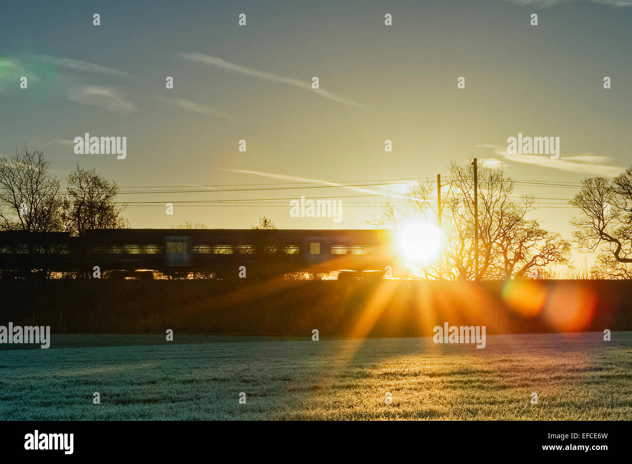 Verschieben von Northern Rail Zug Silhouette gegen steigende Winter Sonne, mit einem frostigen Feld in der ​Foreground. Stockfoto