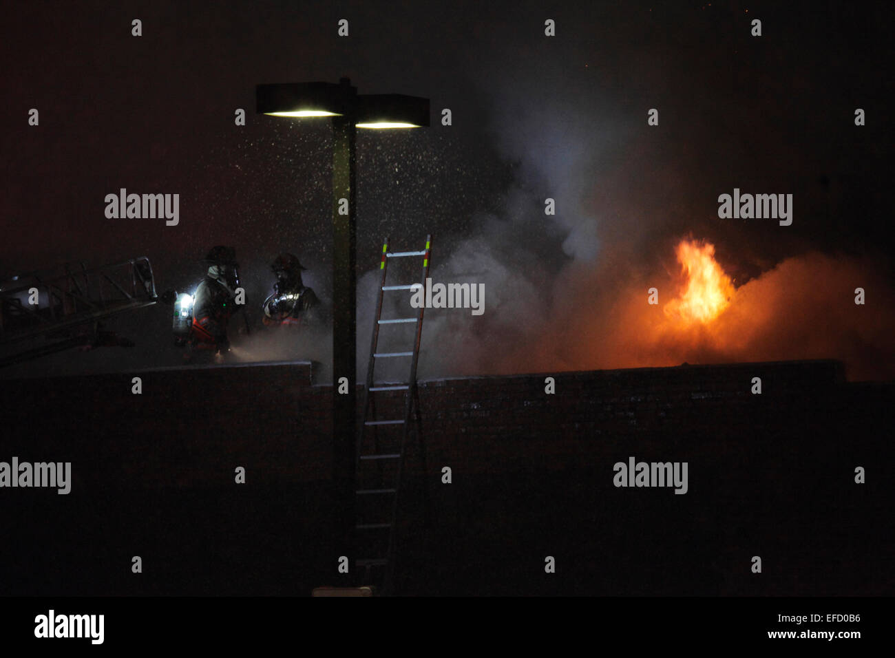 Feuerwehrleute stehen auf dem Dach eines brennenden Buildingas, die Flammen ausbrechen aus der Struktur zu beginnen. Stockfoto