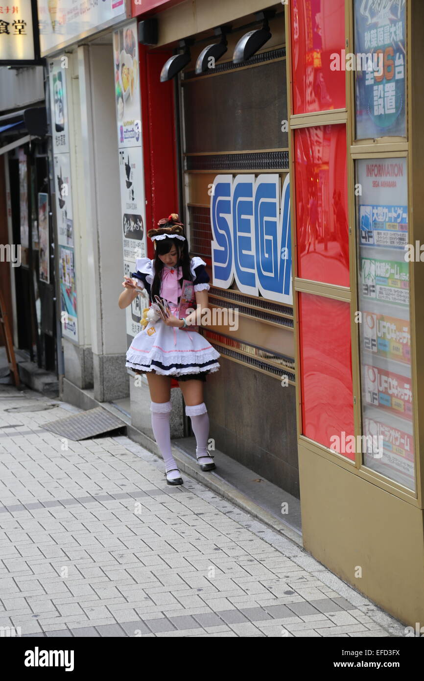 Eine japanische Frau gekleidet wie eine Magd ihr Handy in Akihabara, Japan überprüft. Stockfoto
