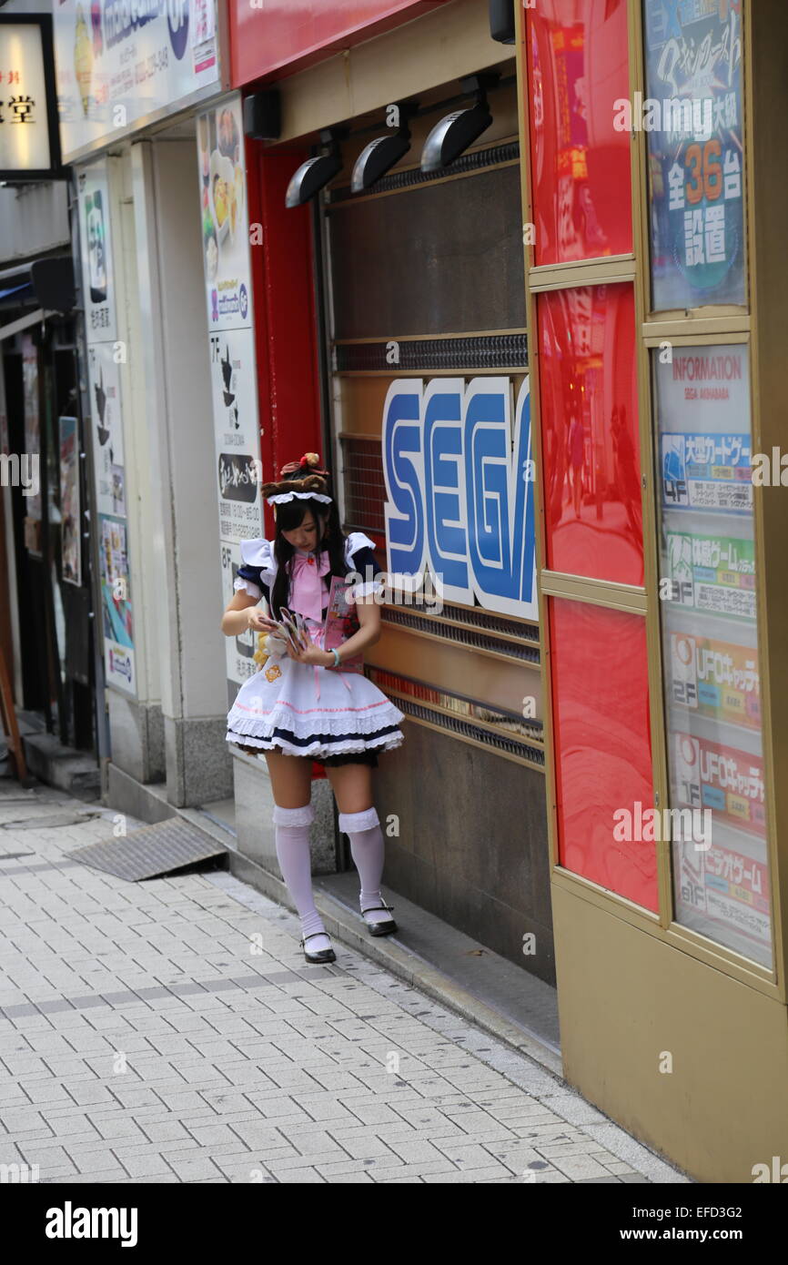 Eine japanische Frau gekleidet wie eine Magd ihr Handy in Akihabara, Japan überprüft. Stockfoto