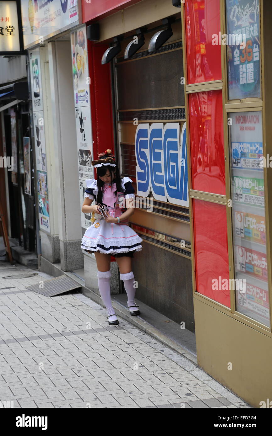 Eine japanische Frau gekleidet wie eine Magd ihr Handy in Akihabara, Japan überprüft. Stockfoto