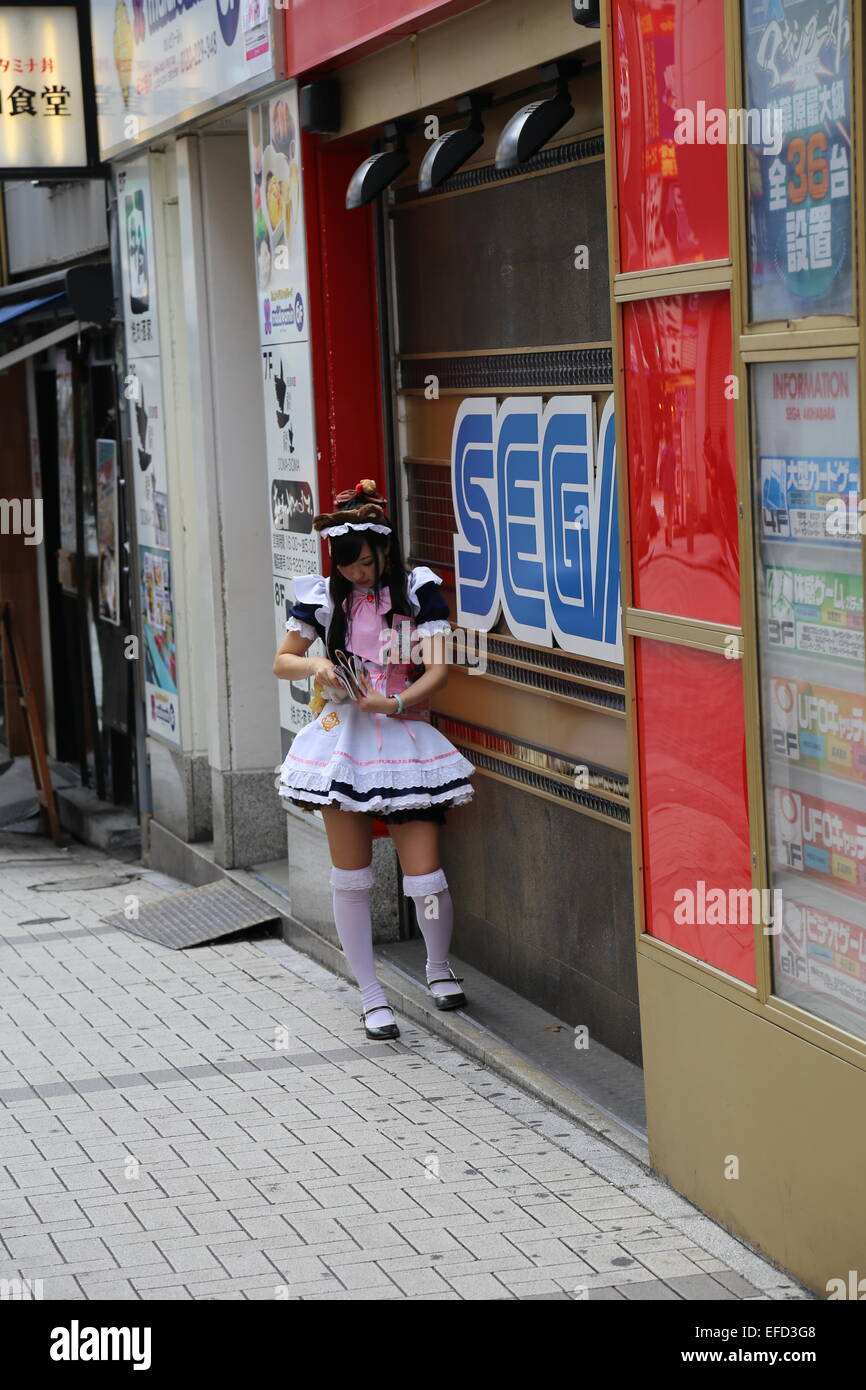 Eine japanische Frau gekleidet wie eine Magd ihr Handy in Akihabara, Japan überprüft. Stockfoto