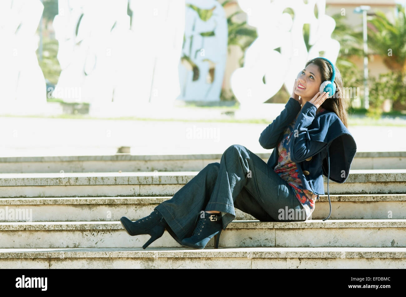 ein Mädchen sitzt auf einer Treppe mit Spaß Musikhören Kopfhörer in Instagram Ton Stockfoto