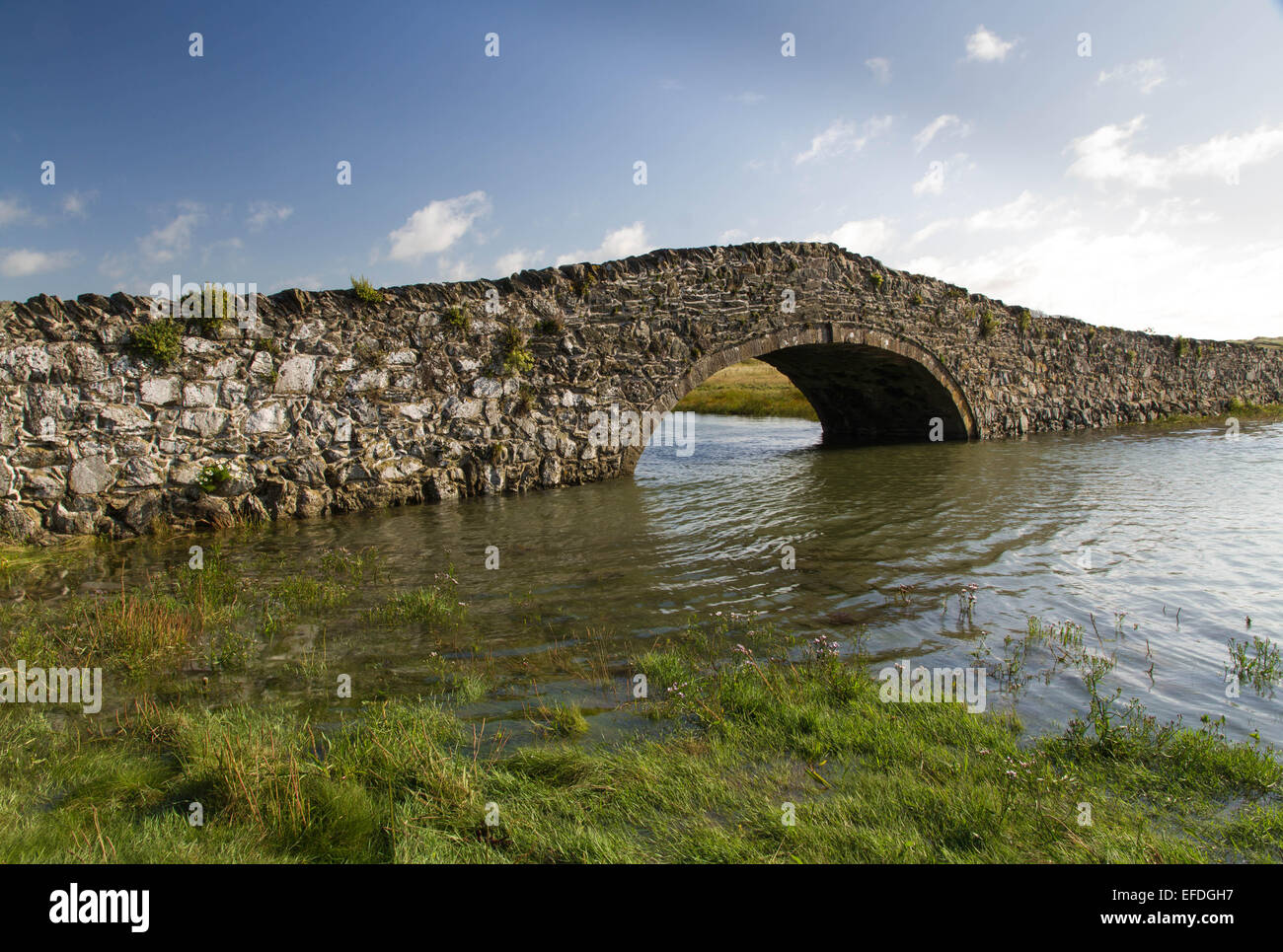 Achtzehnten Jahrhunderts Buckel Stein hintere Brücke mit Wasser Kanal und blauer Himmel. Aberffraw, Anglesey, Wales, Vereinigtes Königreich, Europa Stockfoto