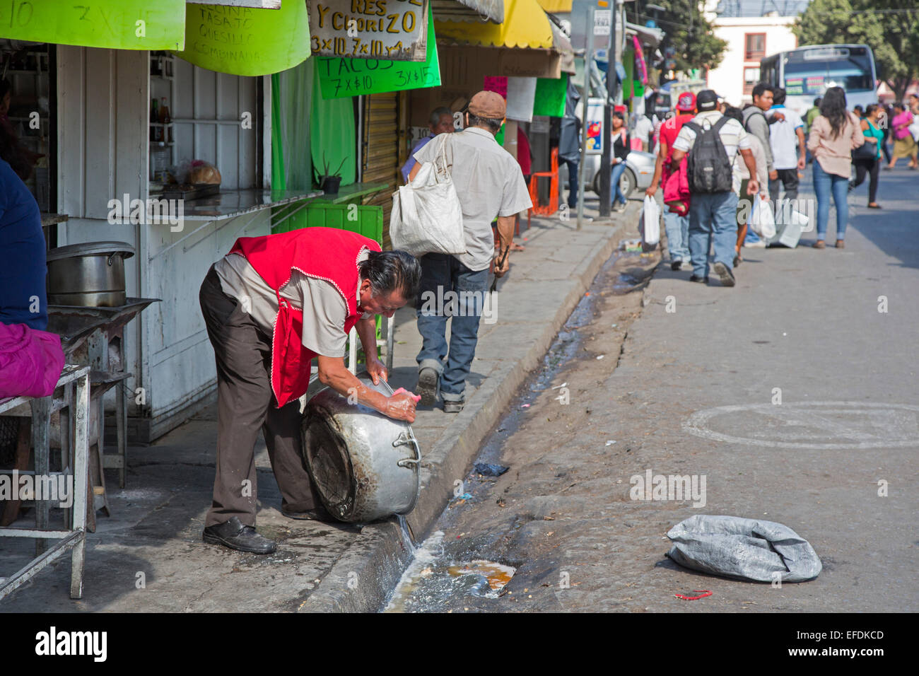 Oaxaca, Mexiko - ein Mann wäscht einen Kochtopf auf der Straße in der Nähe von einem großen öffentlichen Markt. Stockfoto
