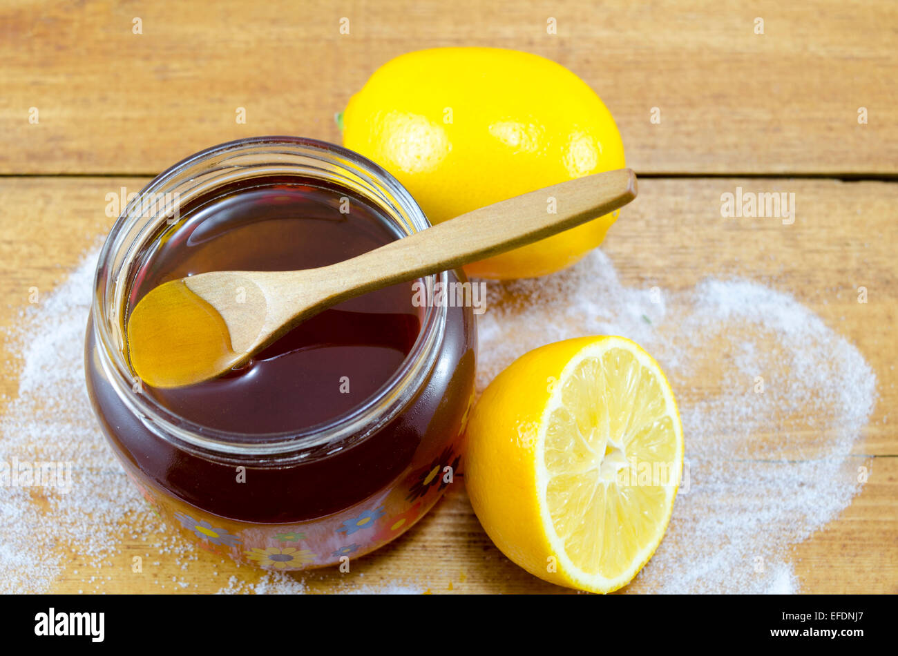 Glas mit dunklem Honig einen Holzlöffel und Zitronen auf einem Tisch Stockfoto