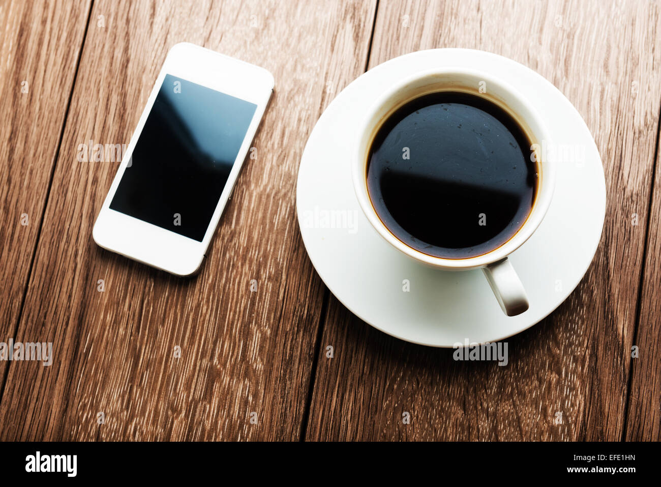 Smartphone und Kaffeetasse auf hölzernen Hintergrund. Stockfoto