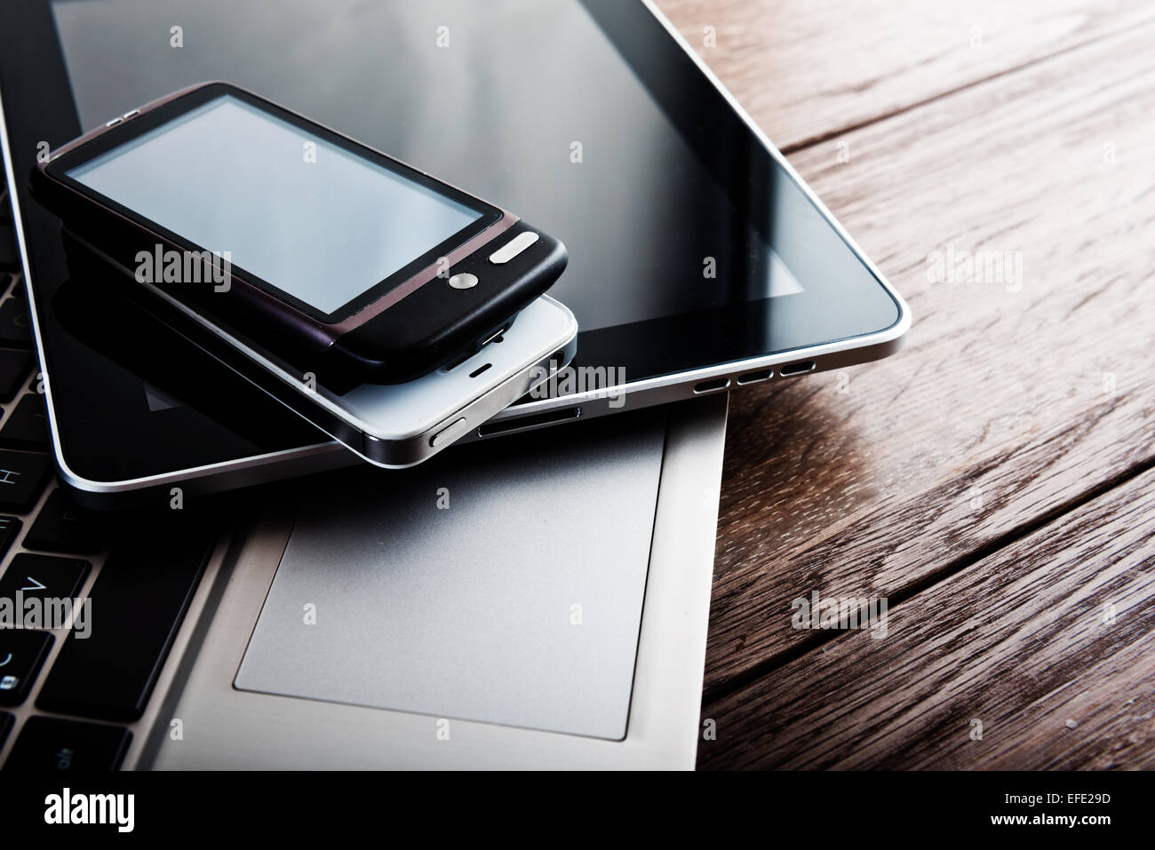 Tastatur mit zwei Handys und Tablet-pc am Schreibtisch aus Holz Stockfoto