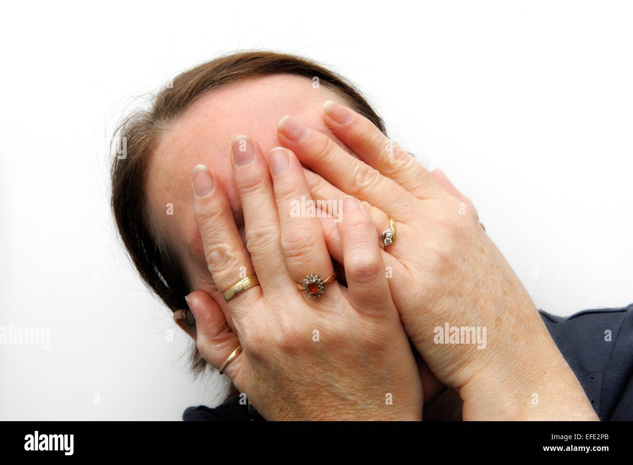 Eine weiße Erwachsenfrau versteckt ihr Gesicht mit beiden Händen Stockfoto