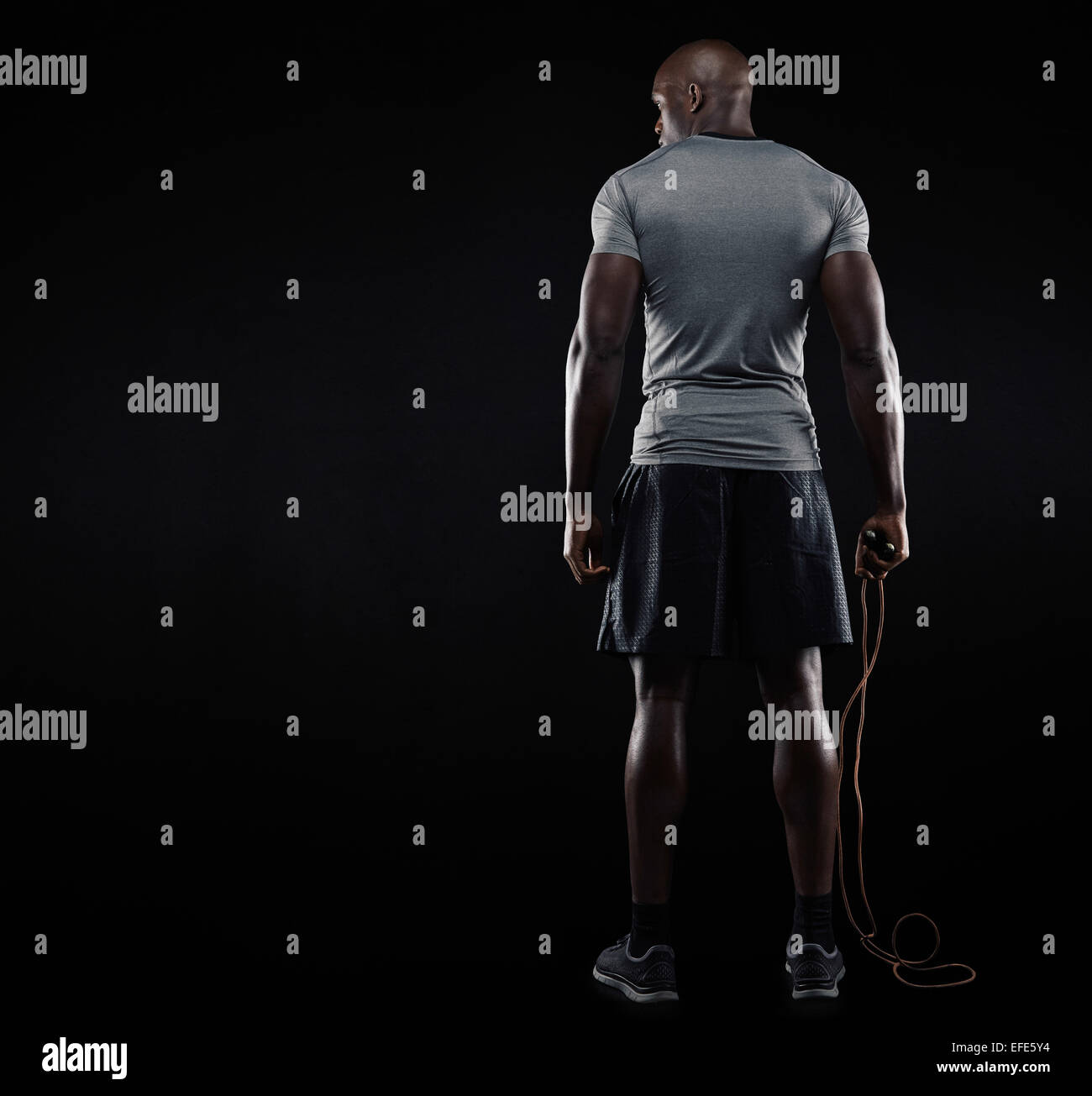Heckansicht des muskulösen Mann stehend mit Seilspringen auf schwarzem Hintergrund. Studioaufnahme von Fitness-Modell halten skipping Rope loo Stockfoto